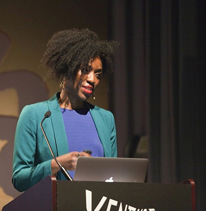 portrait of a woman with a green coat giving a speech
