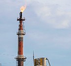 A tall industrial flare stack emits a bright flame against a cloudy sky, highlighting oil refinery operations and combustion processes.