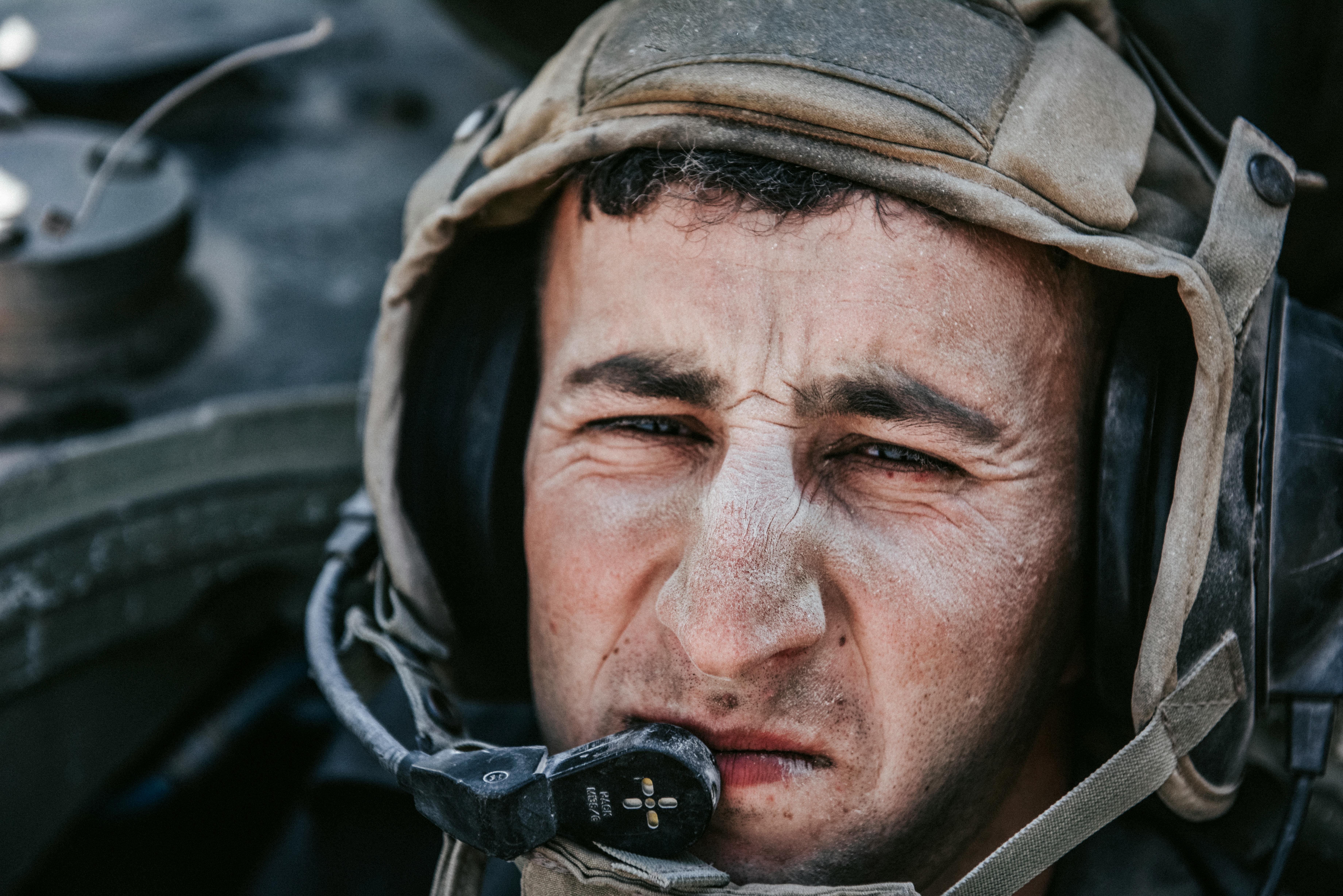 A tank crew member with a dirty face looks at me, only his head in a helmet is visible.