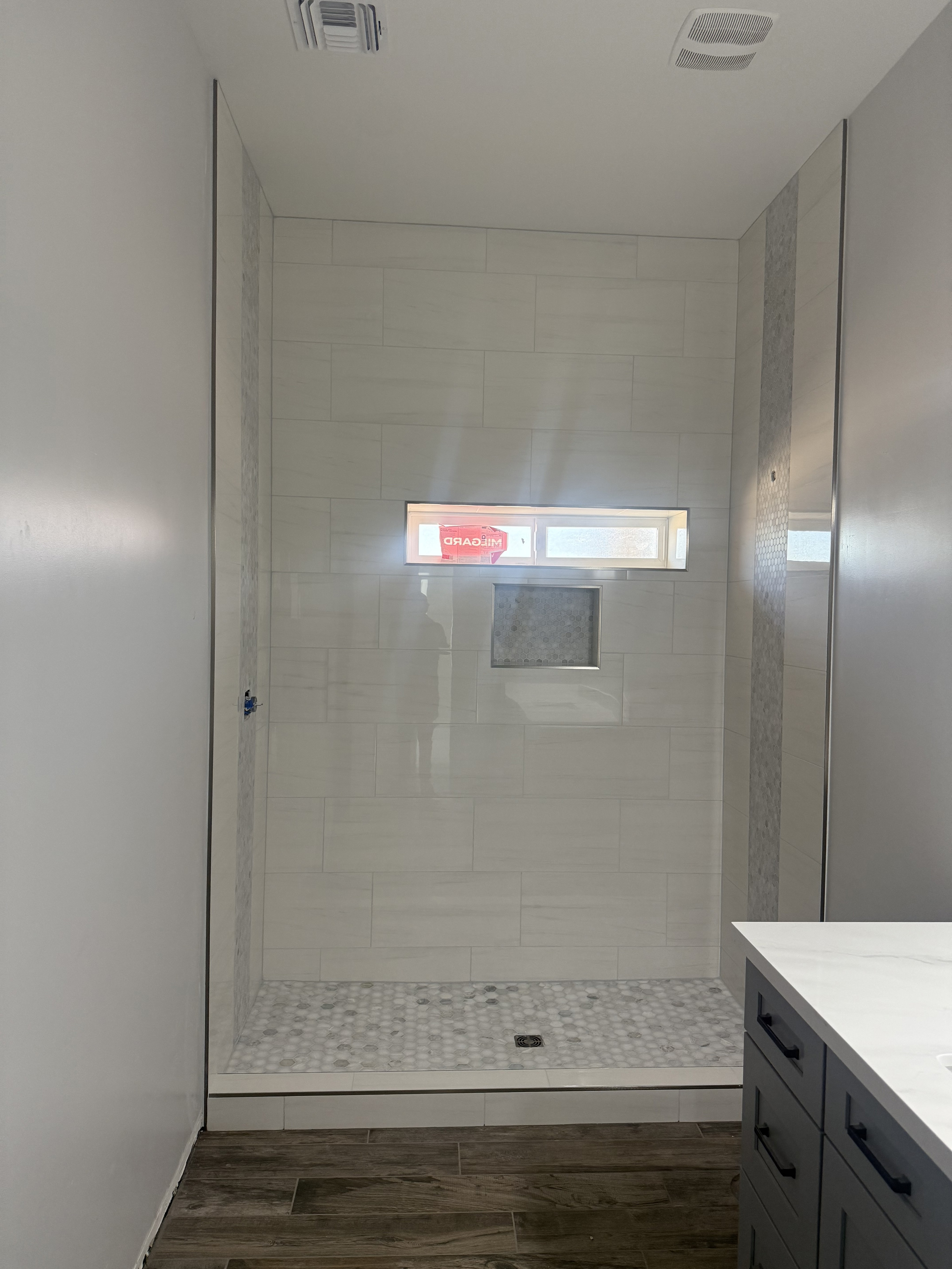 Close-up of a shower niche featuring a vibrant blue and black shattered glass or pebble mosaic tile insert, framed by light beige natural stone wall tiles.