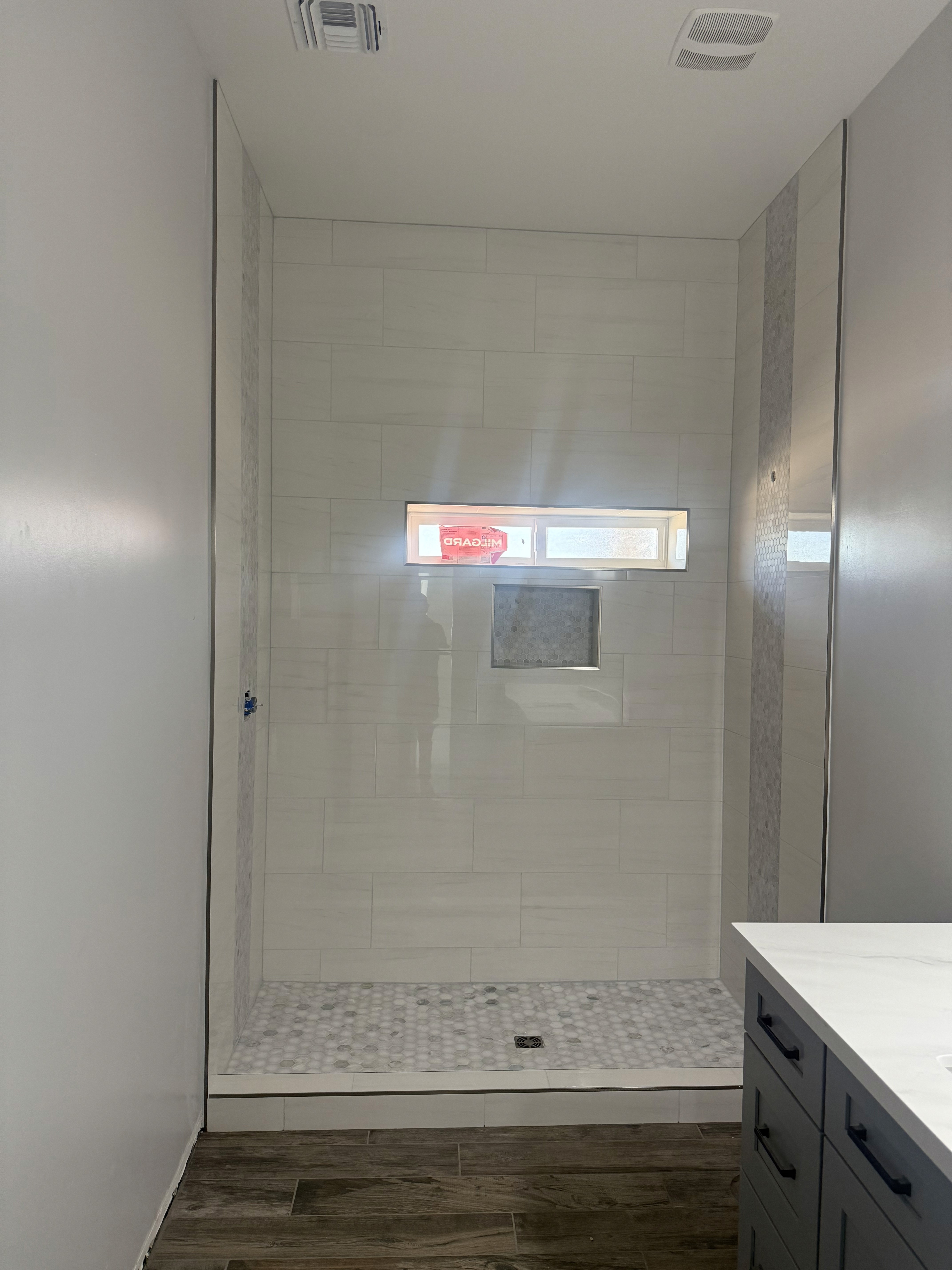 Close-up of a shower niche featuring a vibrant blue and black shattered glass or pebble mosaic tile insert, framed by light beige natural stone wall tiles.