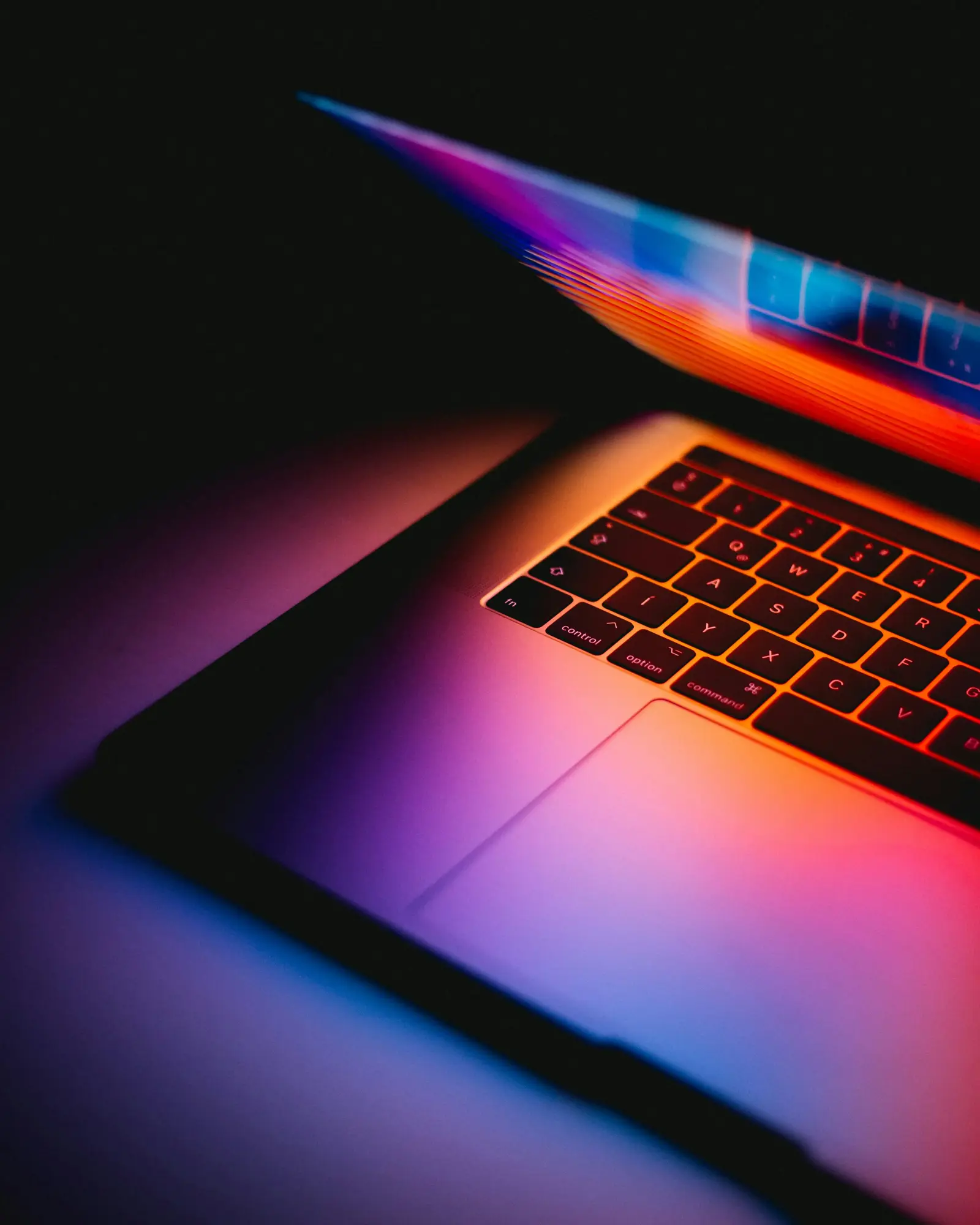 A close-up of a laptop with a colorful illuminated keyboard against a dark background.