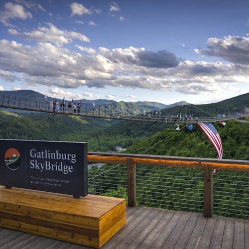 אנשים צועדים על גשר סקייברידג' בגטלינבורג, גשר תלוי ארוך בהרים. שלט כותב: "גשר סקייברידג' בגטלינבורג."