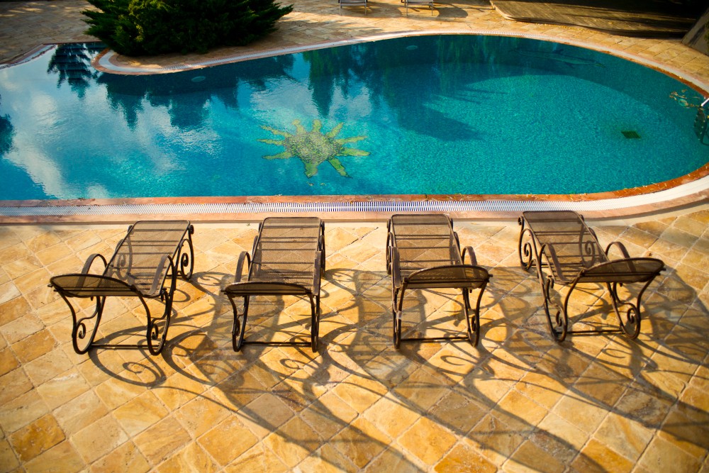 Outdoor pool with decorative tile design on the floor, surrounded by metal sun loungers on a terracotta patio.