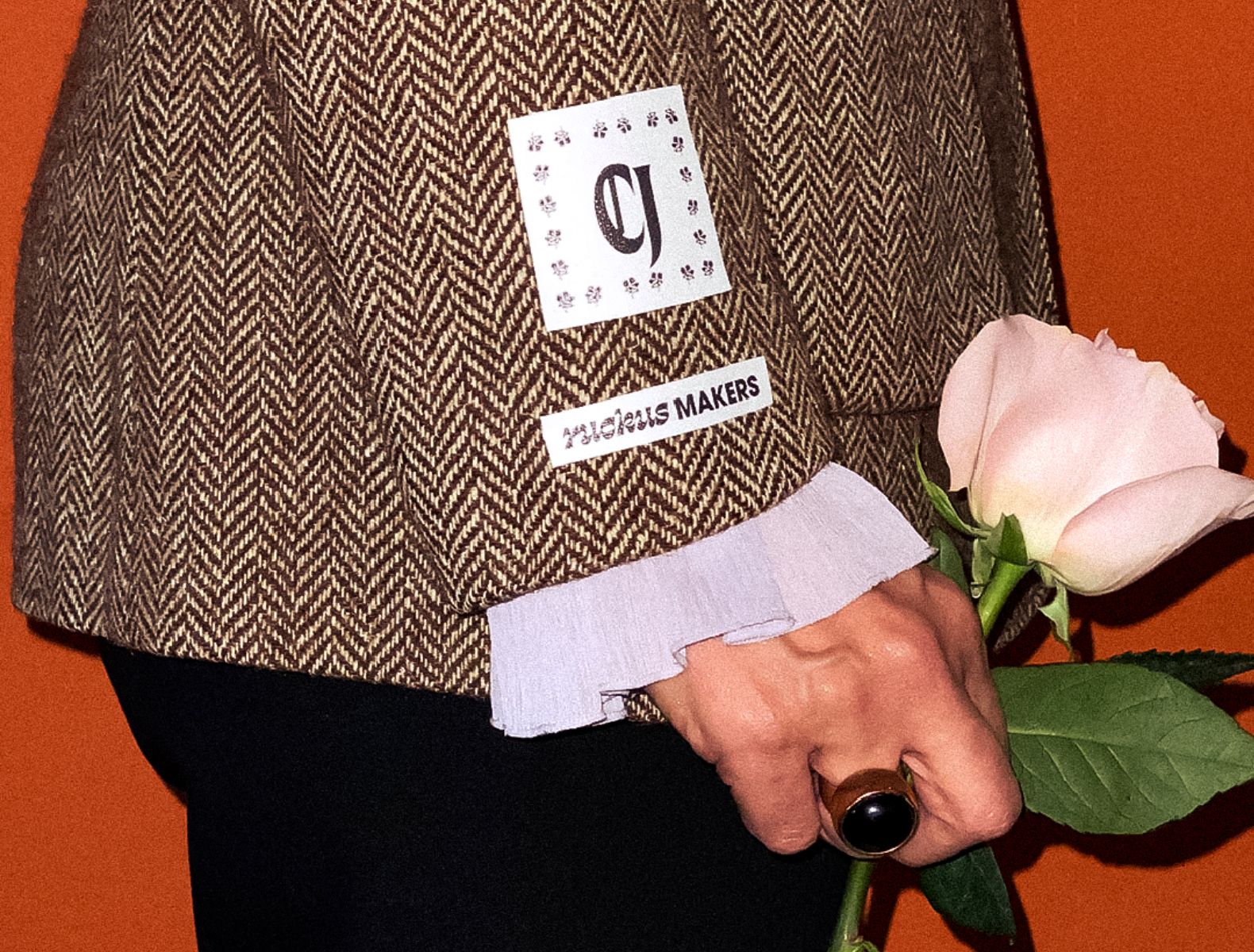 A woman holding a rose wearing a blazer with a patch that has the CJ monogram and a second patch that says "Ruckus Maker"