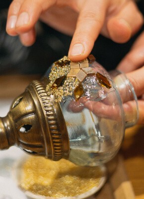 A detailed shot of hands carefully placing mosaic tiles on a glass lamp base, part of a mosaic crafting workshop in Istanbul, highlighting the intricate design process.