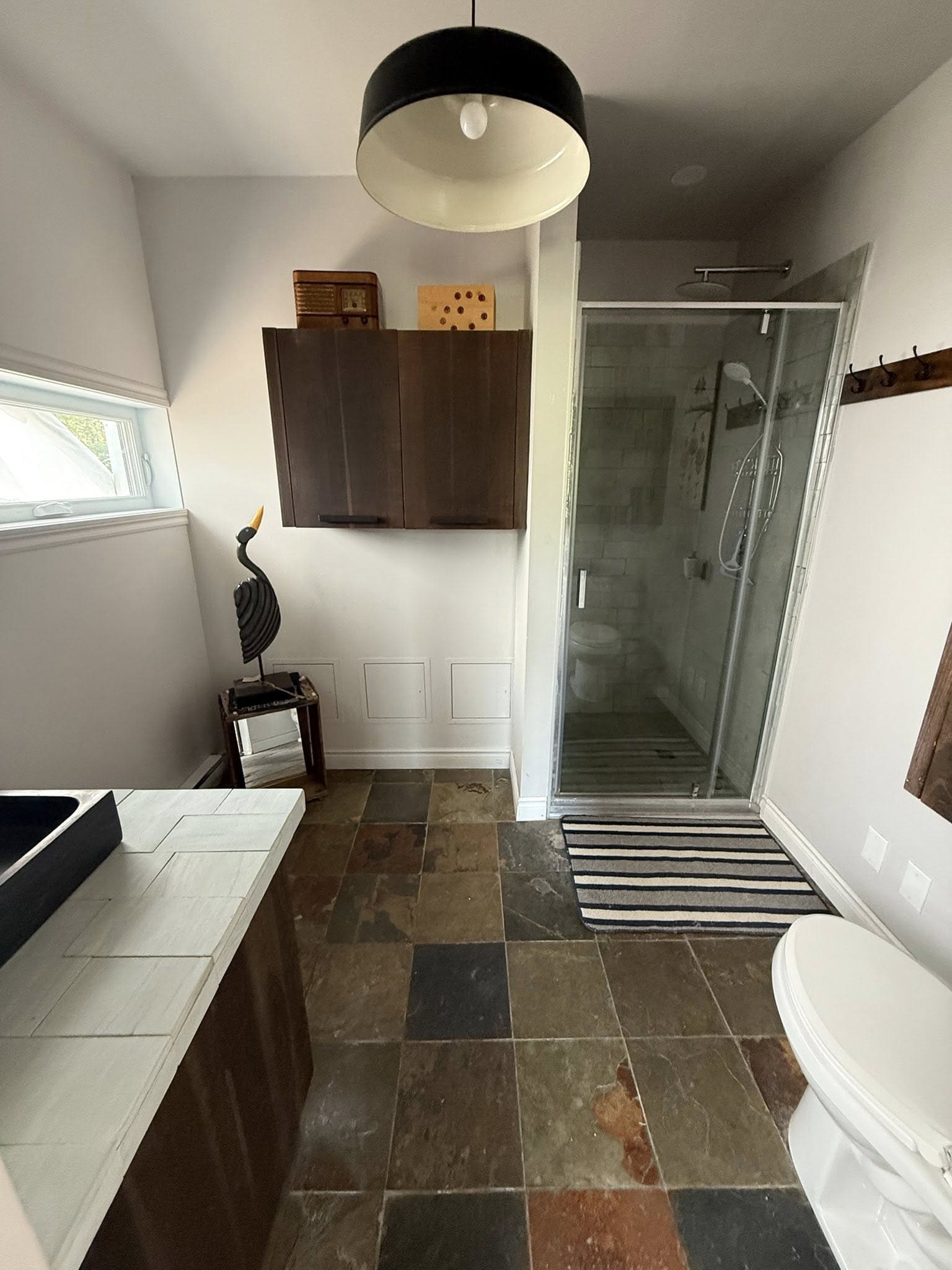 Douche vitrée avec carrelage en ardoise multicolore, lavabo contemporain et rangements en bois foncé.