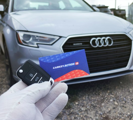 carkeyaction technician holding business card with a car key made for audi in front of the car