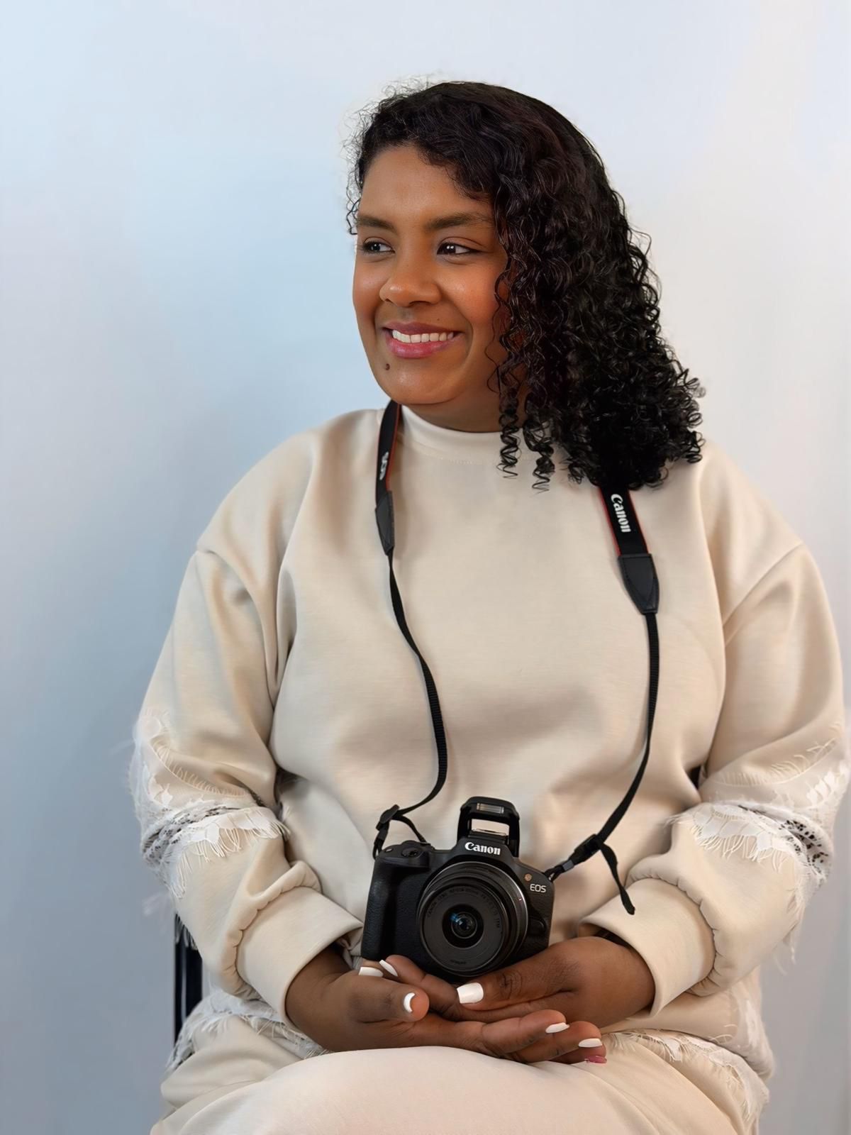 A person with shoulder-length blonde hair wearing a black newsboy cap and a black sweater.