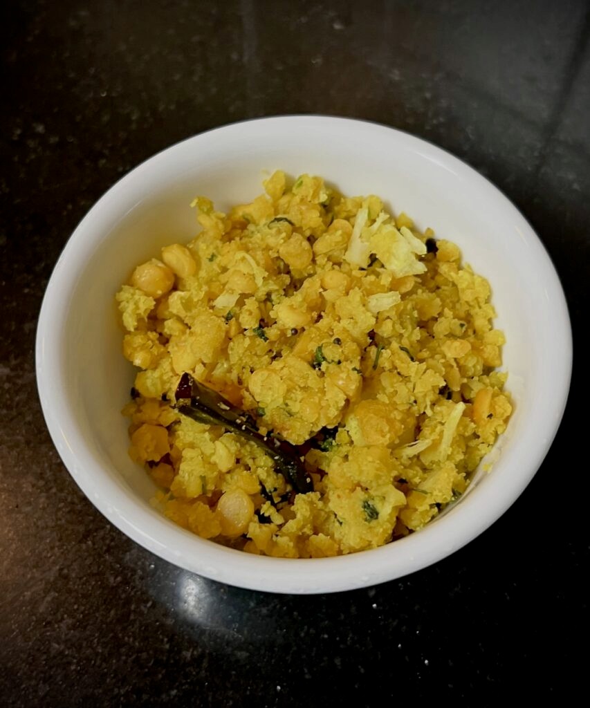 Yellow coloured chana dal and raw mango salad, known as ambe dal. The salad is tempered with red chillies and mustard seeds and garnished with coriander leaves and freshly grated coconut
