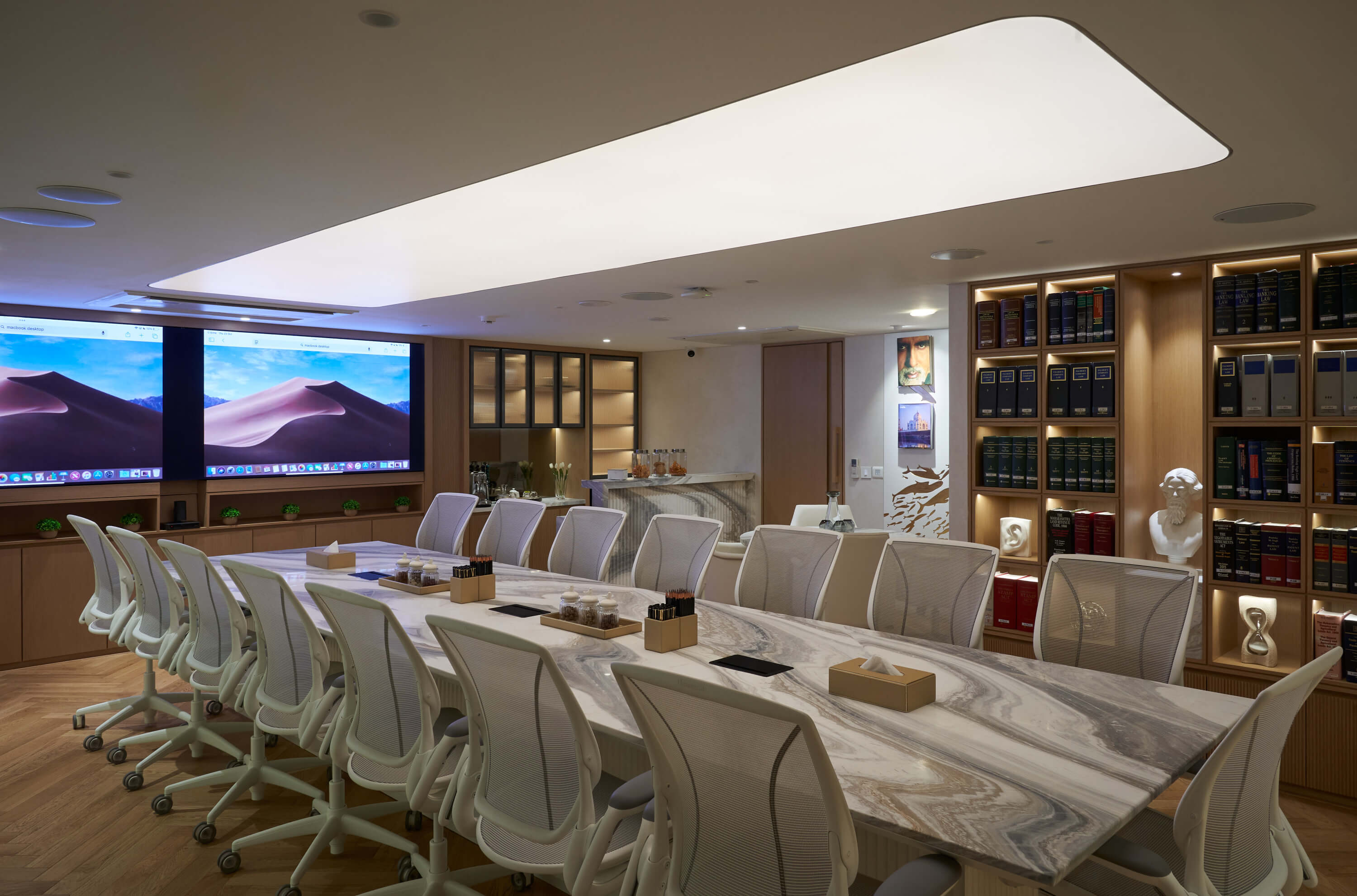 Large boardroom with marble table, white ergonomic chairs, and backlit bookcase wall.