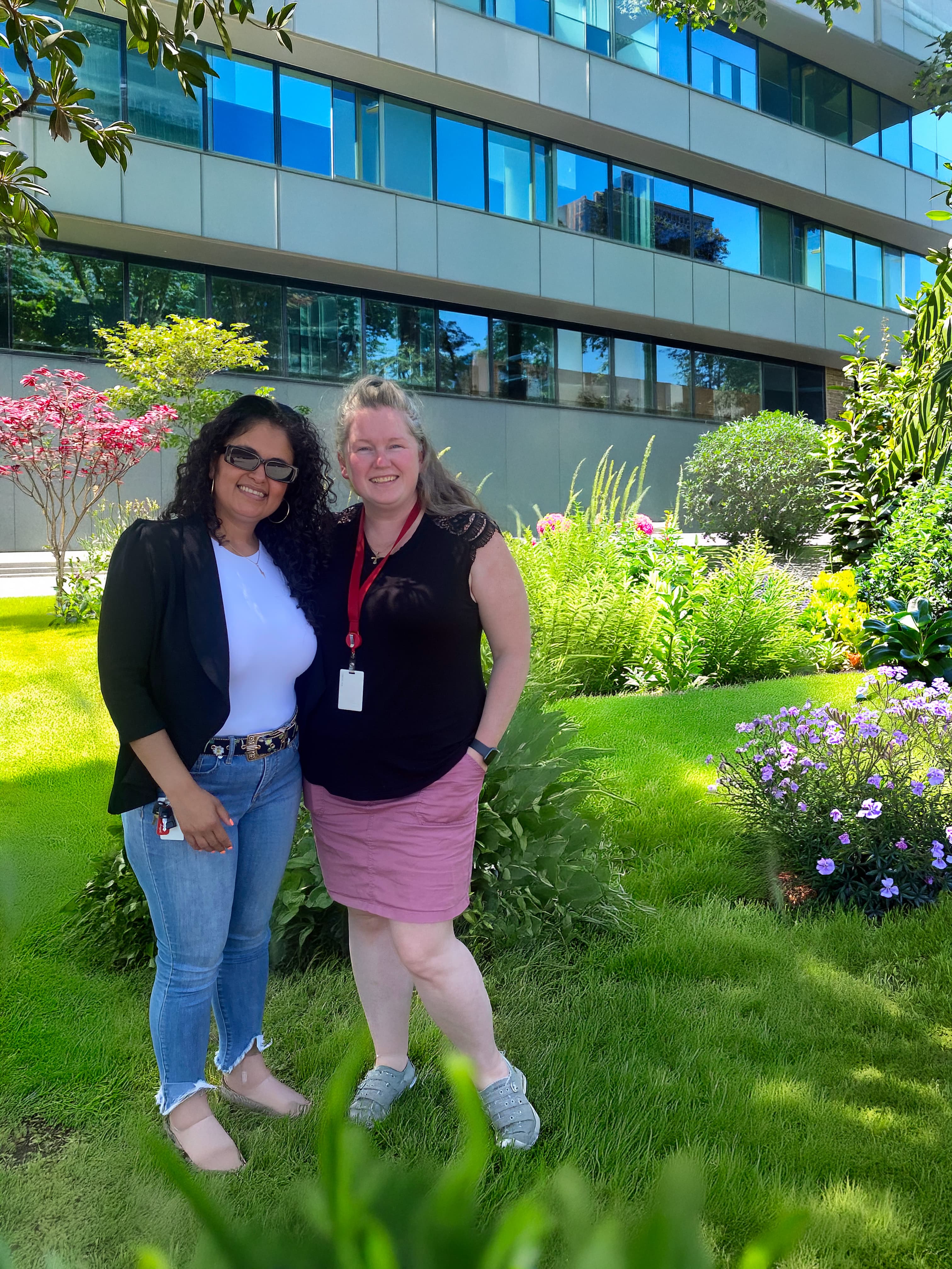 2 Women Standing in front of the building outside by the garden. 