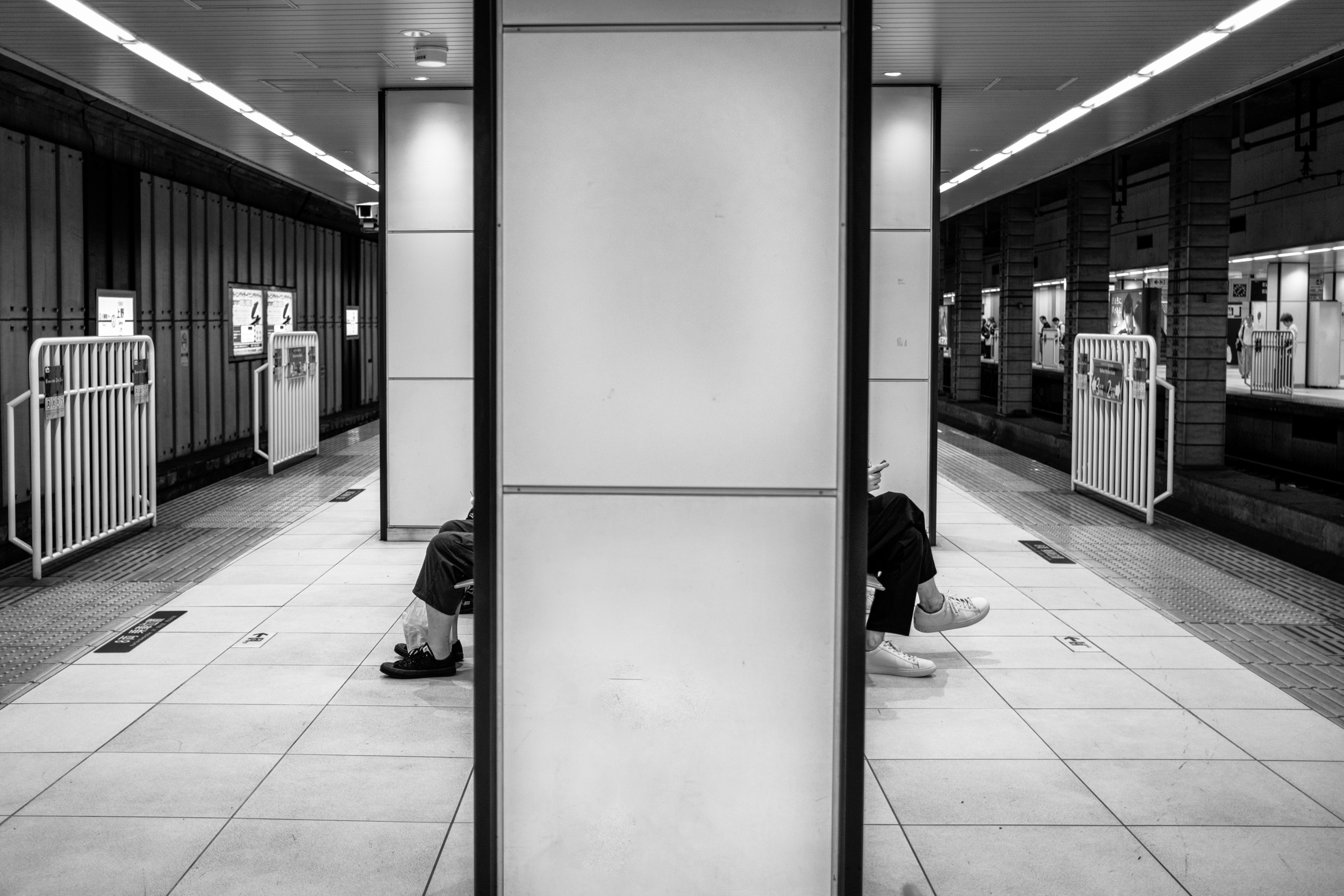Black and white interior subway photograph with legs of seated riders visible on each side of a central pillar.