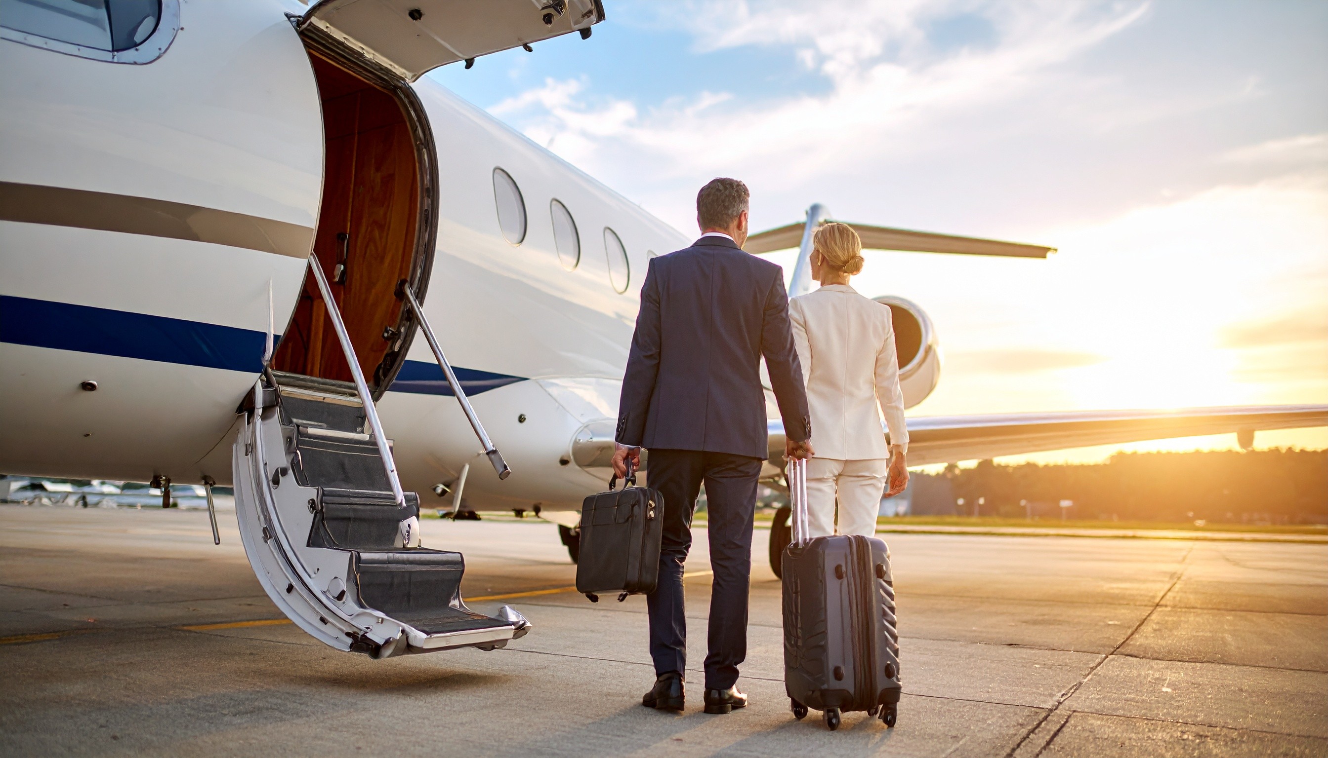 Geschäftsmann und Geschäftsfrau mit Gepäck besteigen bei Sonnenuntergang auf dem Rollfeld einen Privatjet.