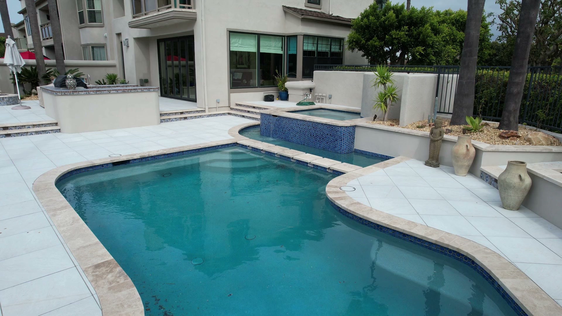 A pool and raised spa beside a light-colored paved deck and home.