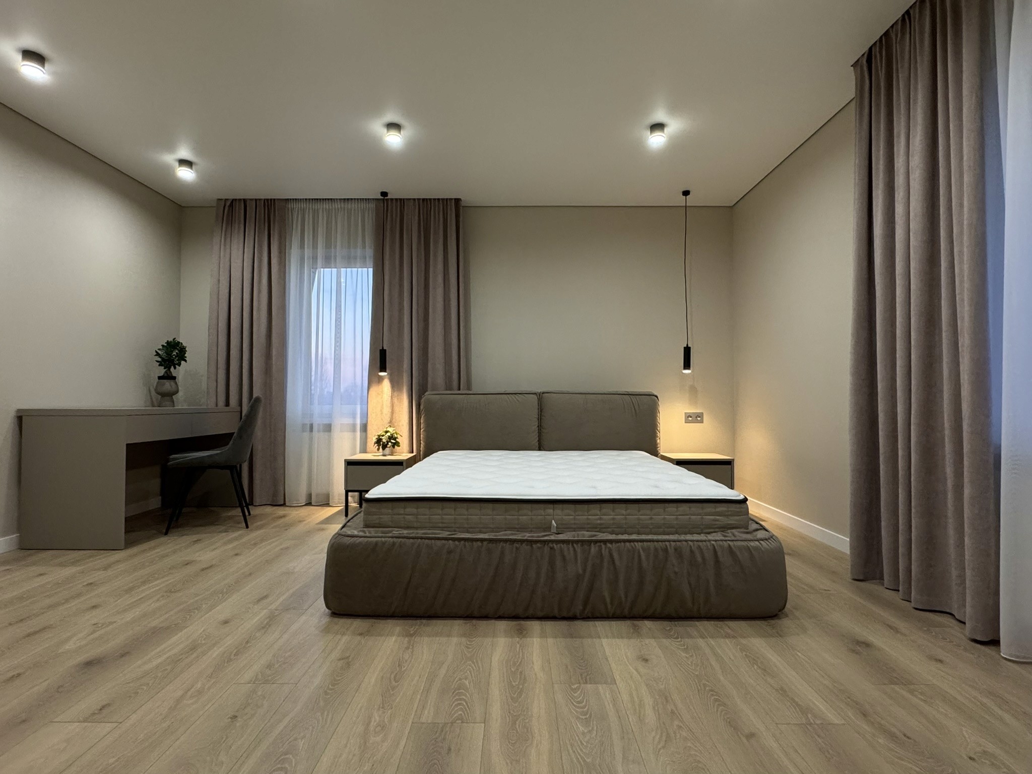 Сучасна спальня з м’яким ліжком, письмовим столом і текстильними шторами