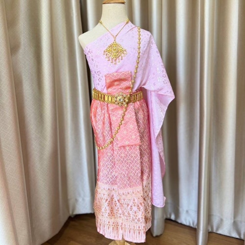 粉色传统服装套在一个模特上，搭配金色配饰，背景是米色窗帘。