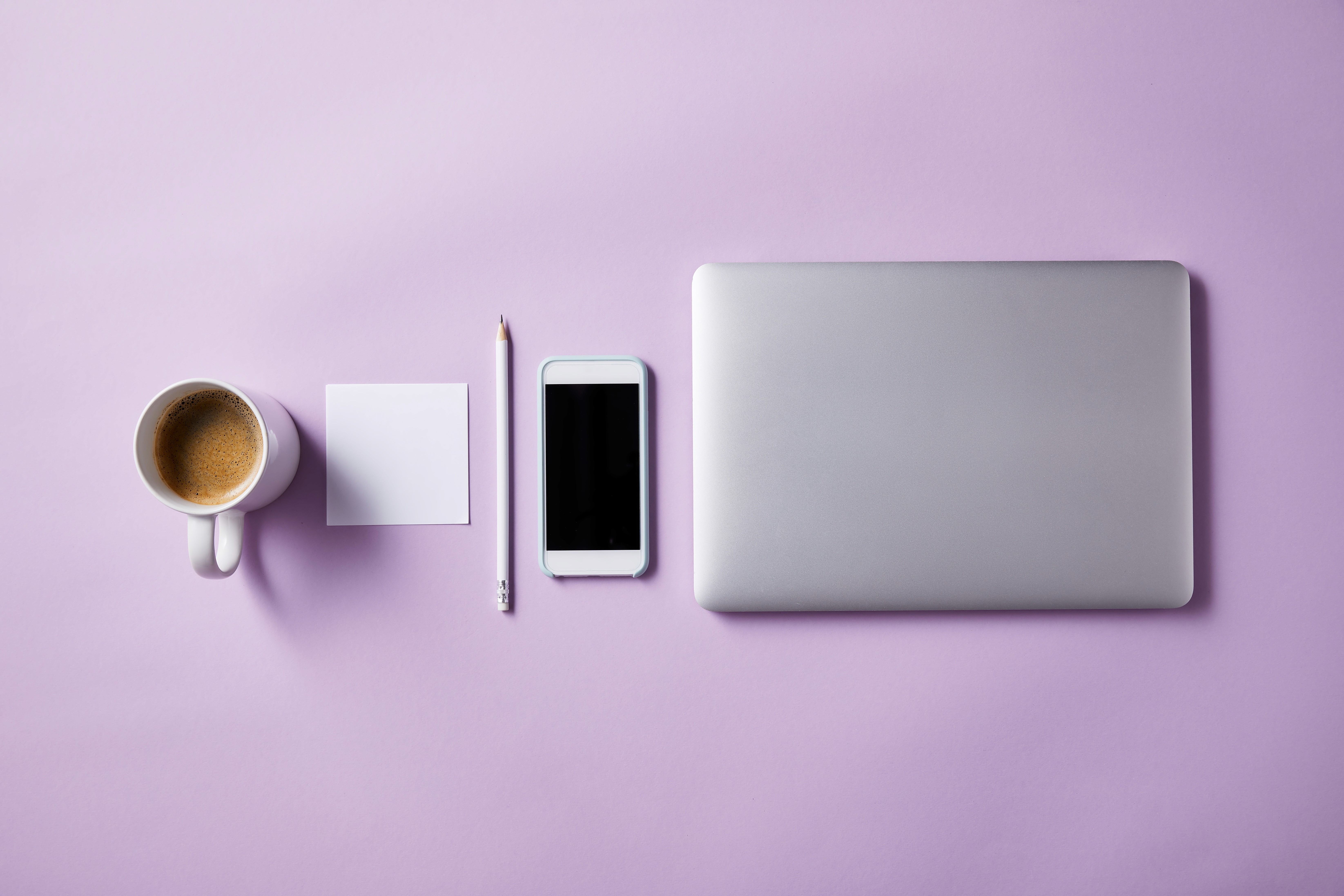 Laptop, phone, notebook and coffee arranged on a lavender desk