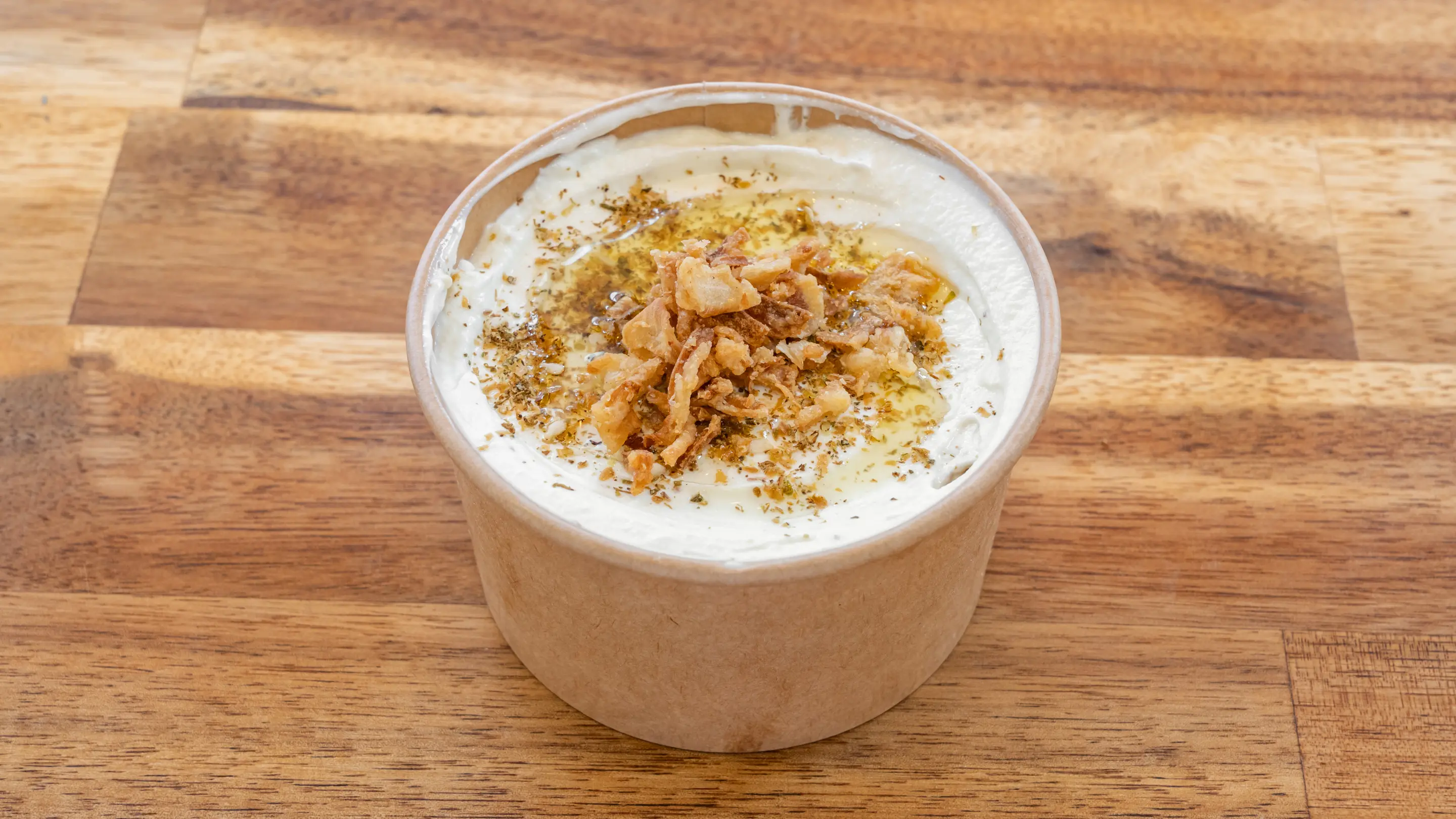 Labné dans un pot kraft avec un filet d’huile d’olive, zaatar et oignons frits