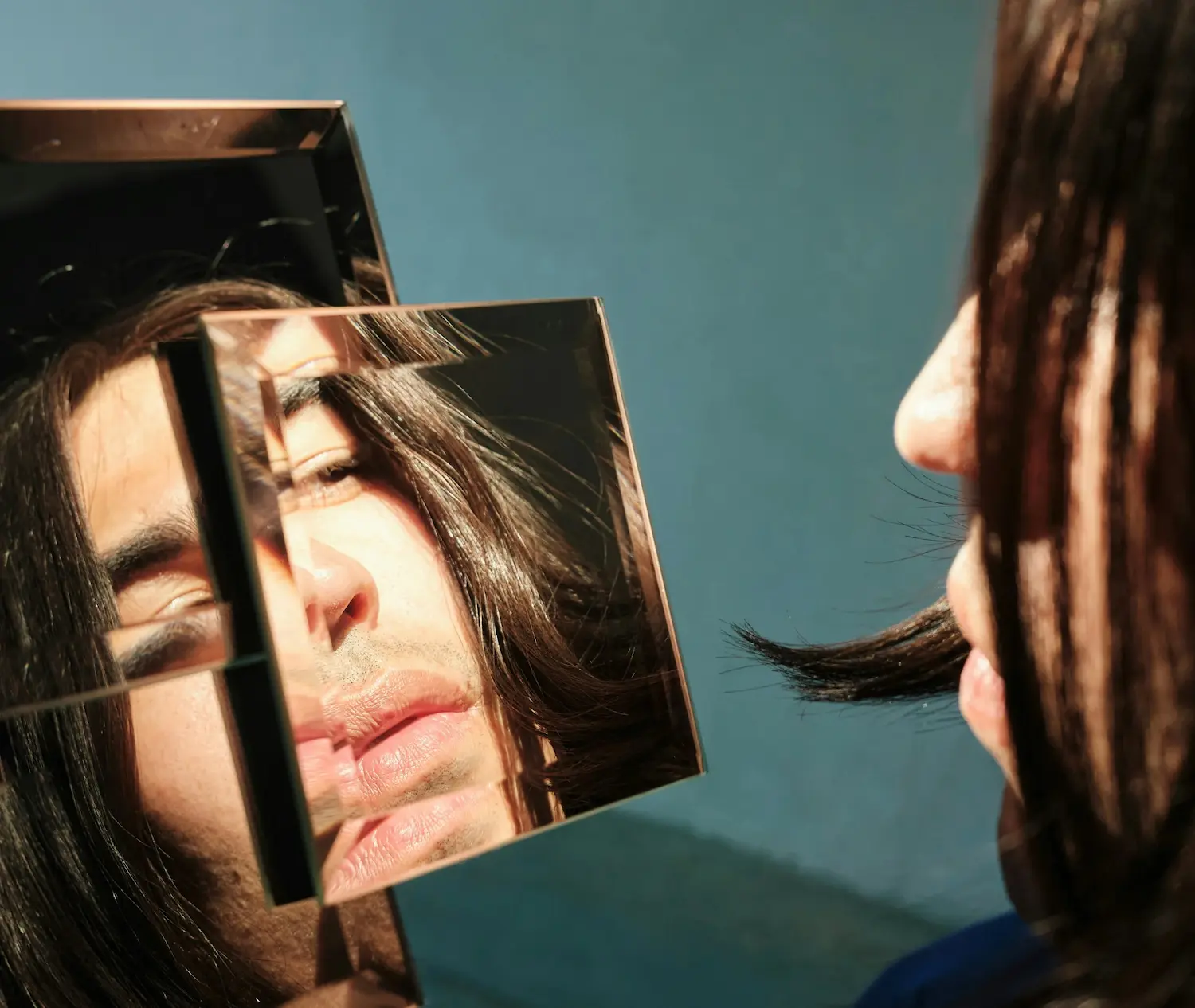 Person looking into a fragmented mirror that reflects distorted parts of their face, symbolizing body image concerns, self-perception, and identity.