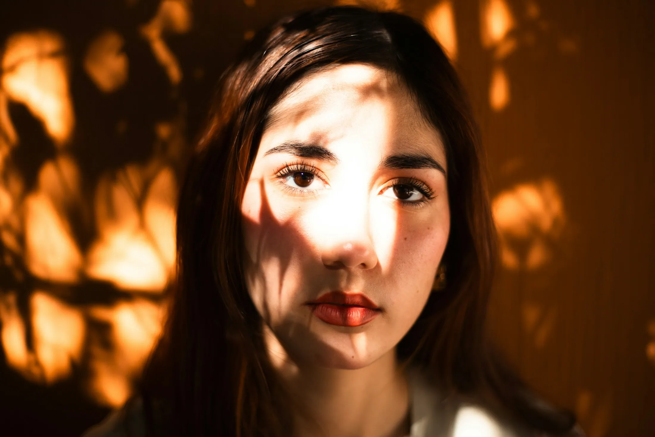 A woman's face crossed by leaf shadows