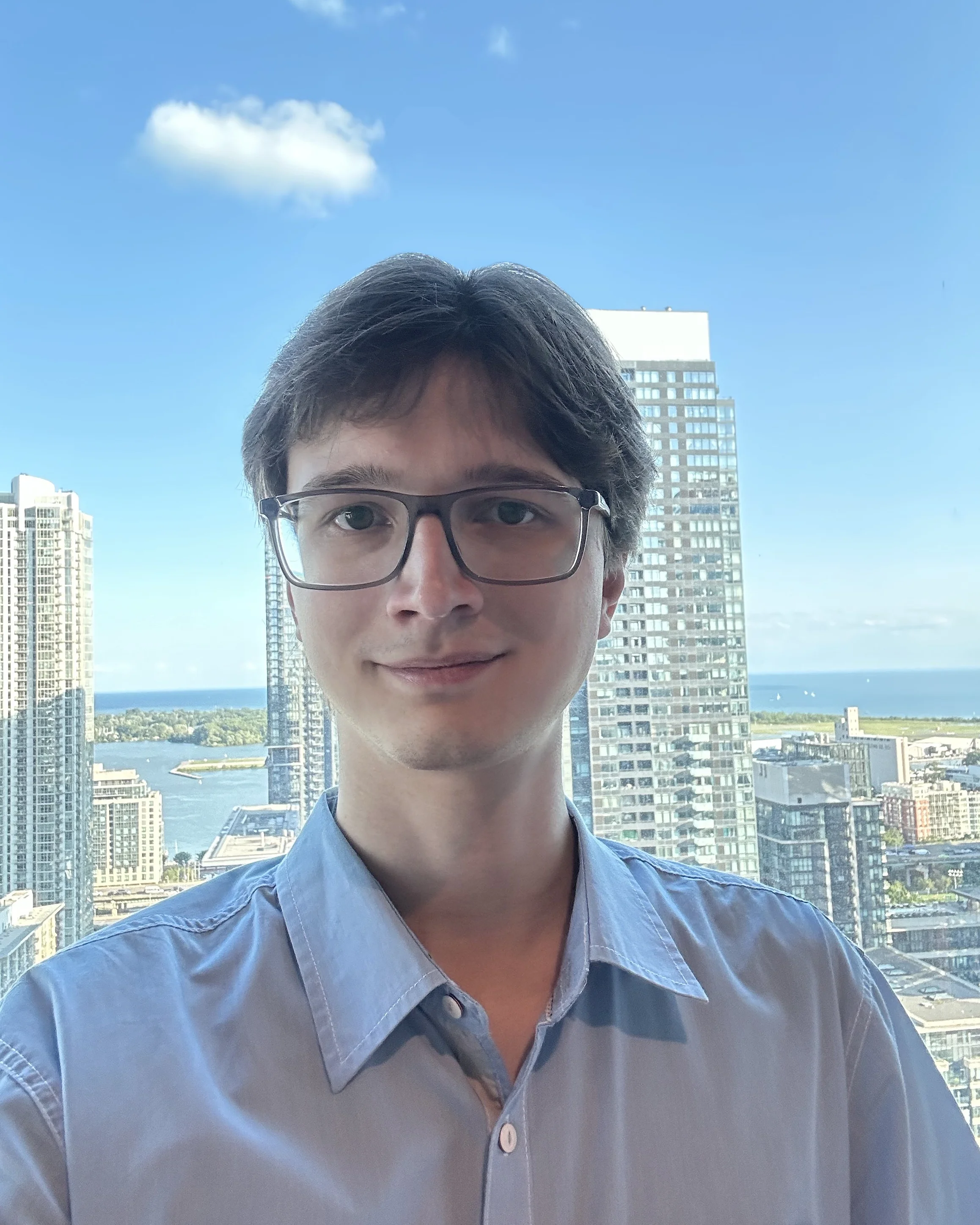 Portrait of Aleksandr, standing with Toronto cityscape in the background.