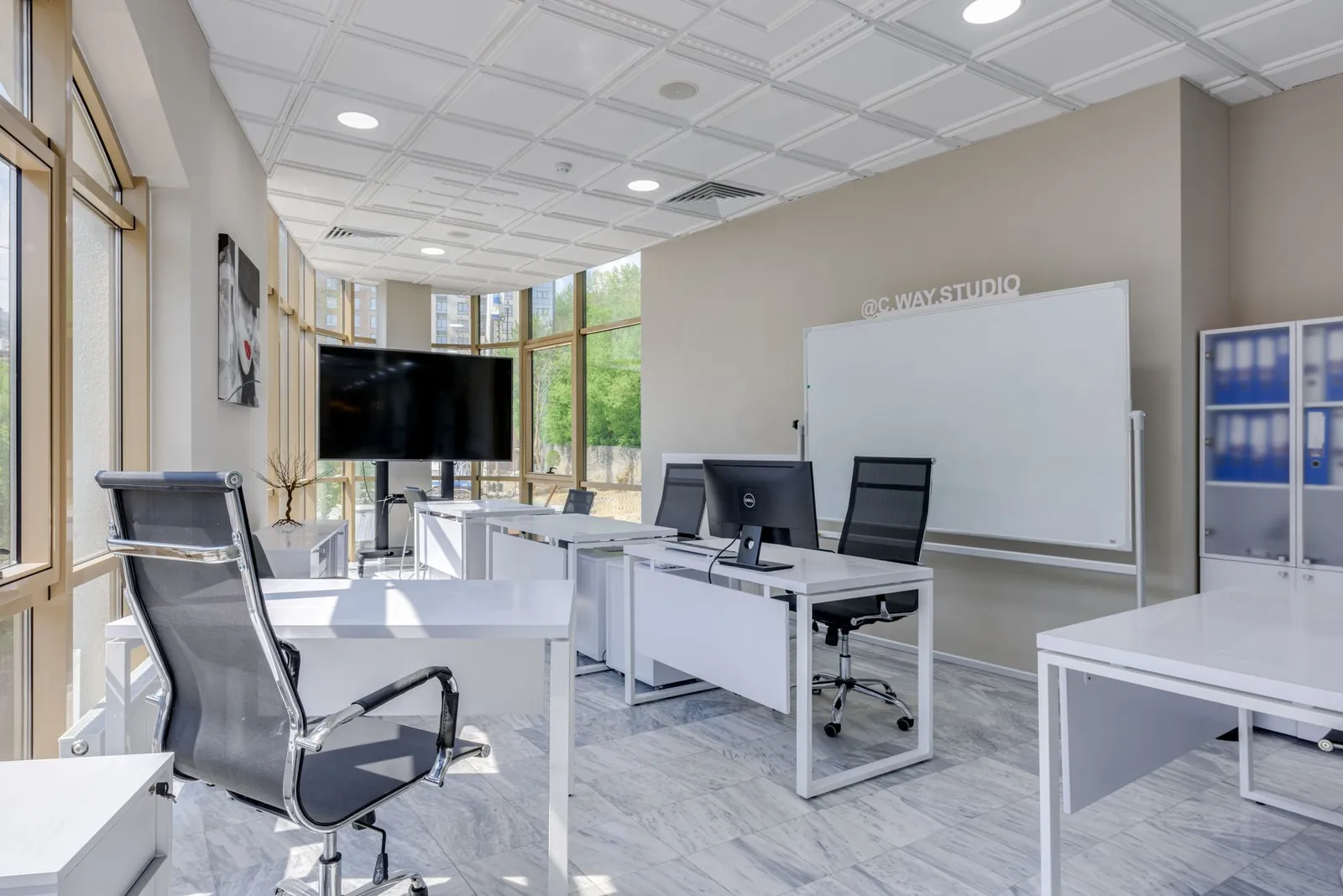 A bright open-plan office with white desks and grey chairs