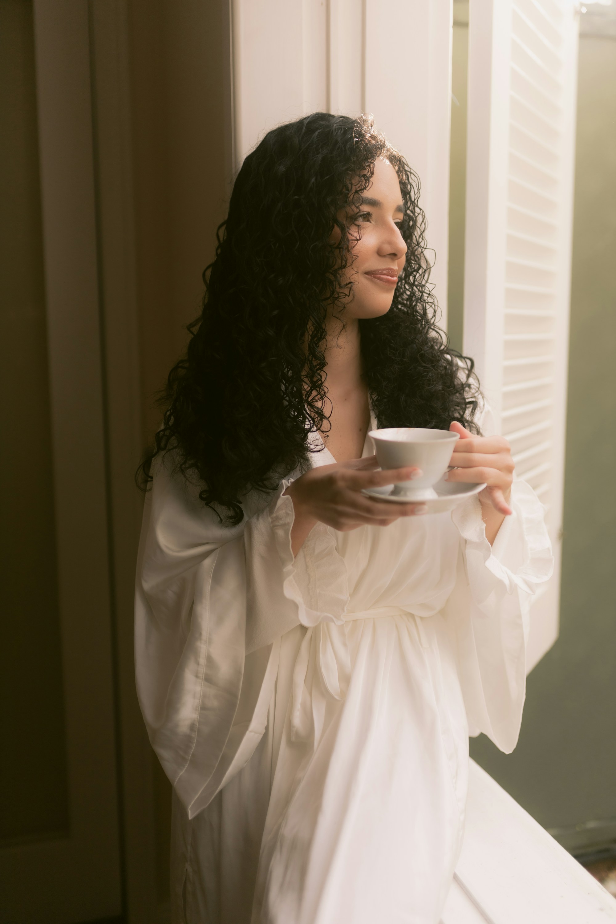 Guest in a soft white robe holding a cup of tea beside a sunlit window