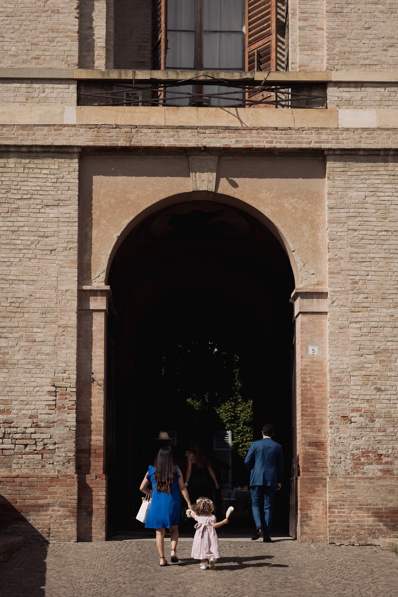 Sposi attraversano l'arco in pietra della Rocca di Soragna, ospiti li seguono nella cerimonia matrimoniale al tramonto