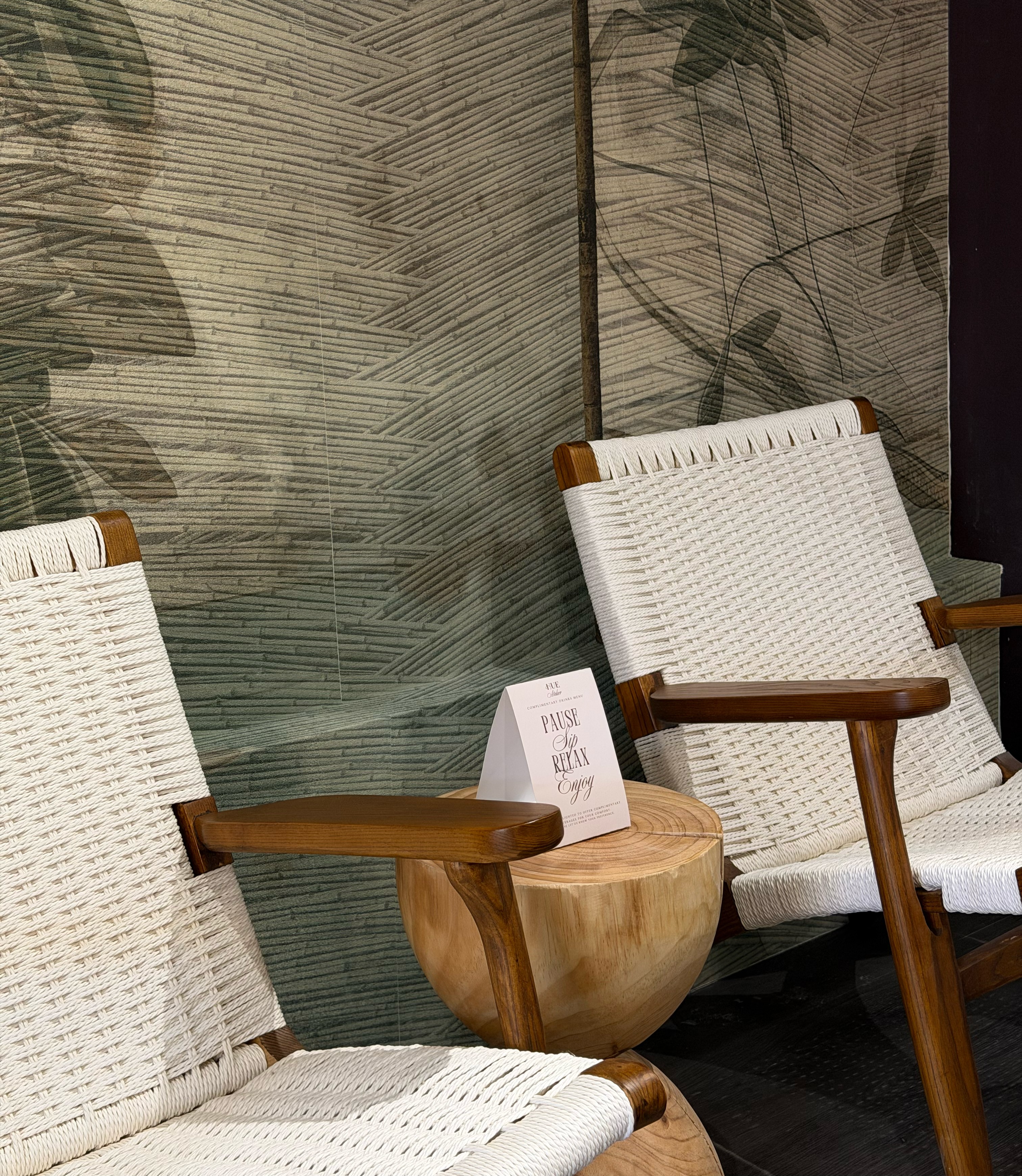 A serene and elegant spa space with wooden reclining chairs and white cushions. Golden sunlight filters through a cascading water feature, creating a peaceful atmosphere. Tropical plants and candles add to the relaxing ambiance.