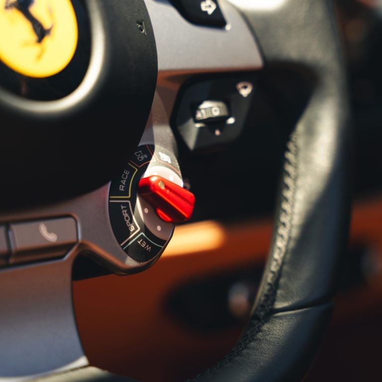 Detailed view of the Ferrari F8 Spyder steering wheel, with the iconic yellow Ferrari emblem and engine start button.