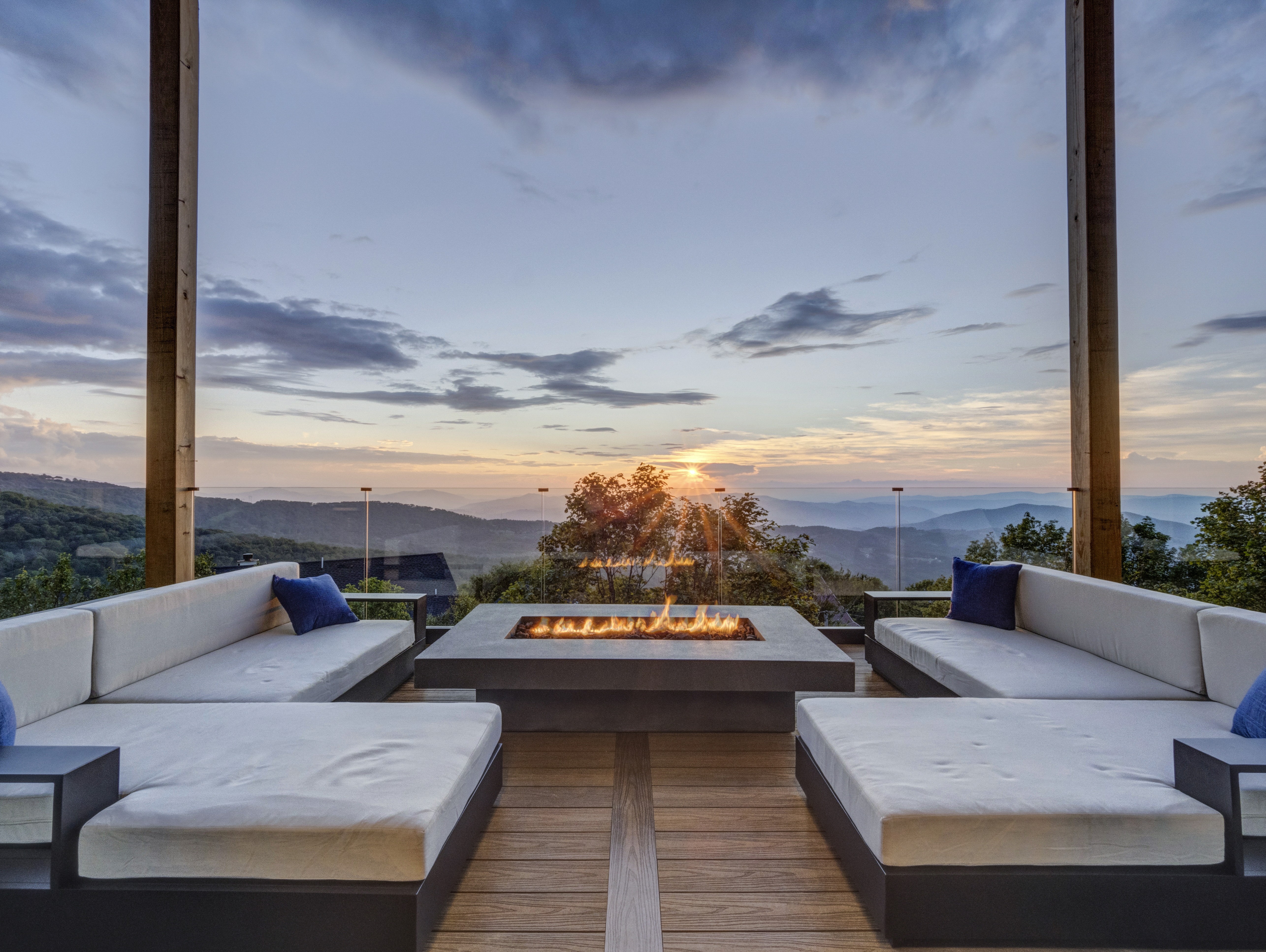 Symmetrical shot of a luxury mountain villa's deck, highlighting the fire pit and contemporary outdoor furniture at sunset