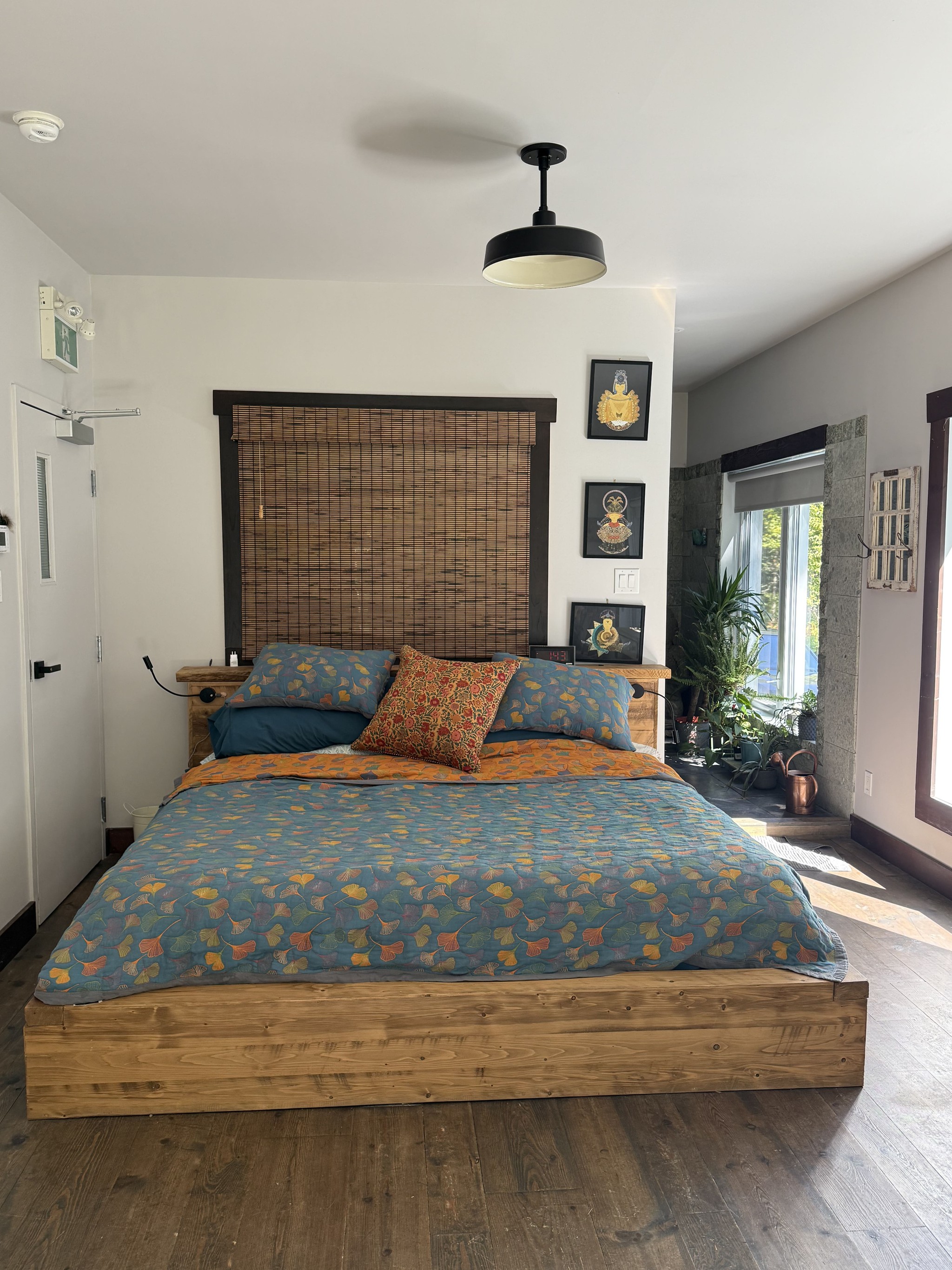 Grand lit en bois avec literie aux motifs de feuilles ginkgo, plancher en bois rustique et grandes fenêtres.