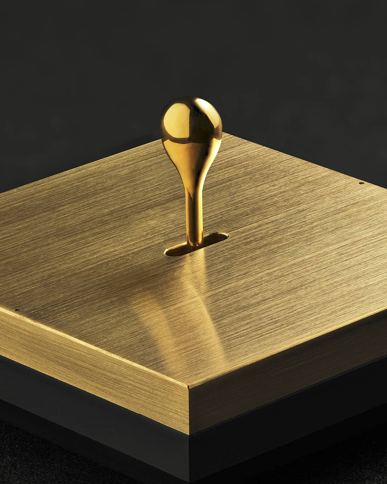 Gold droplet sculpture on brushed gold plate against dark background.