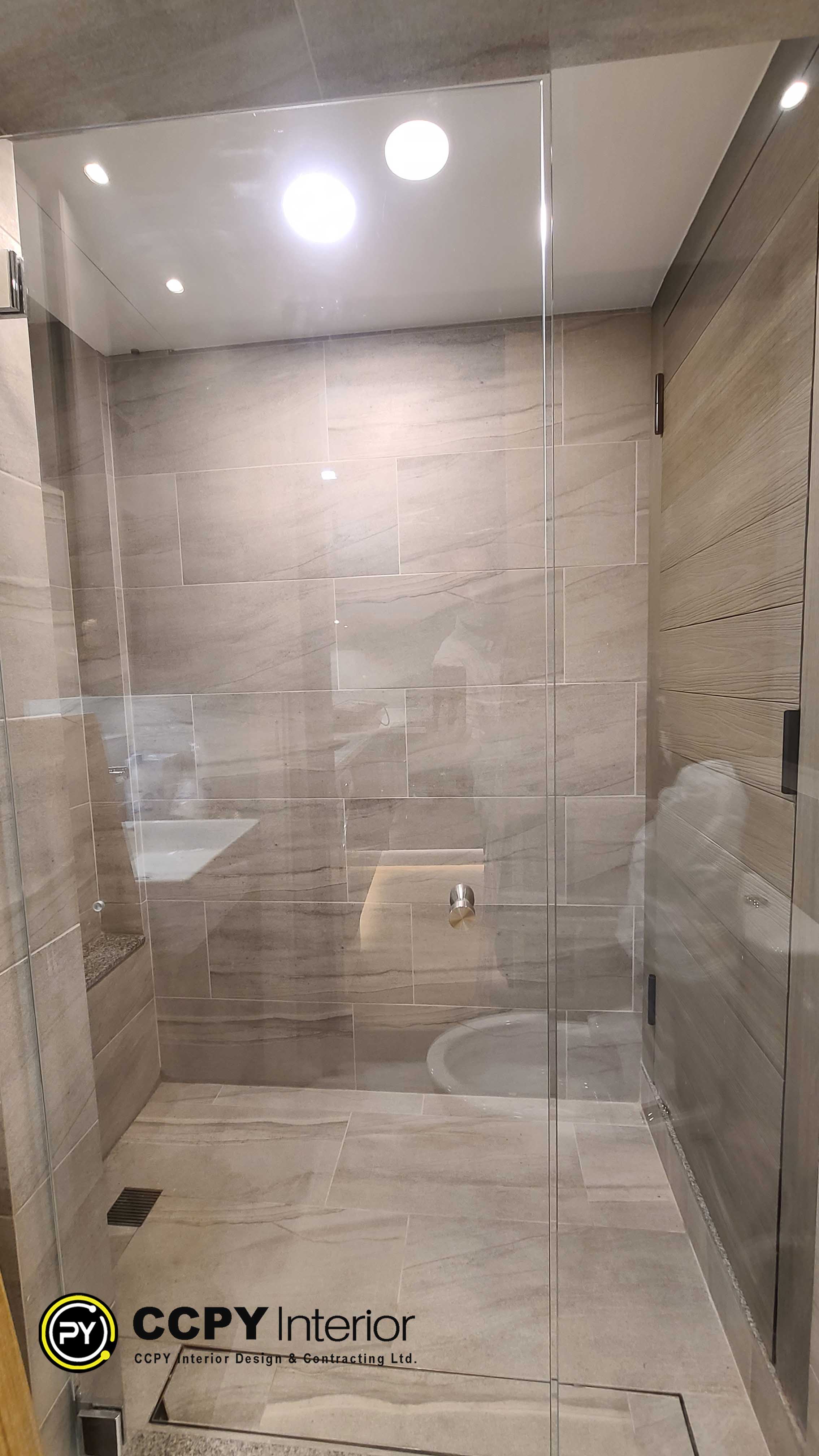 The selected region shows a modern bathroom interior featuring large-format beige or light-taupe wall tiles with subtle horizontal veining, a glass shower enclosure, and light-toned wood-look cabinetry on the right.Key Design FeaturesTiles: Large porcelain or ceramic tiles with stone-like textures.Glass Work: Frameless glass partitions that maximize light flow.Wood Accents: Vertical-grain wooden panels or doors for warmth.