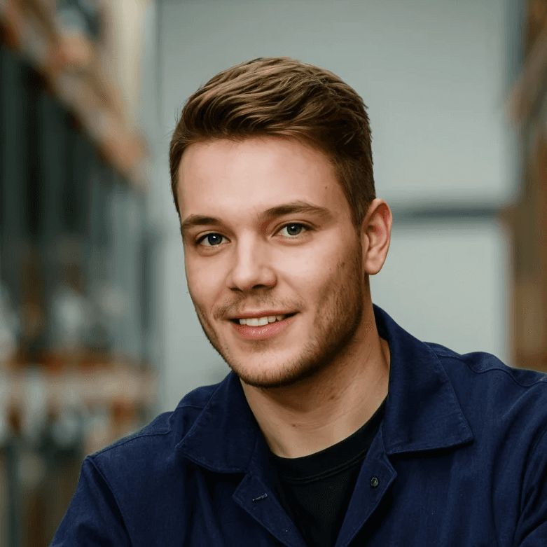 Smiling young man with brown hair wearing a blue work shirt looking at the camera.