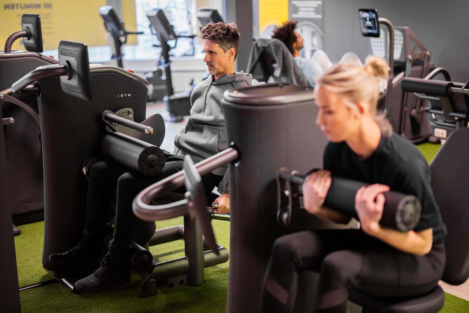 Two individuals are exercising in a hub, using fitness equipment with a focus on strength training.