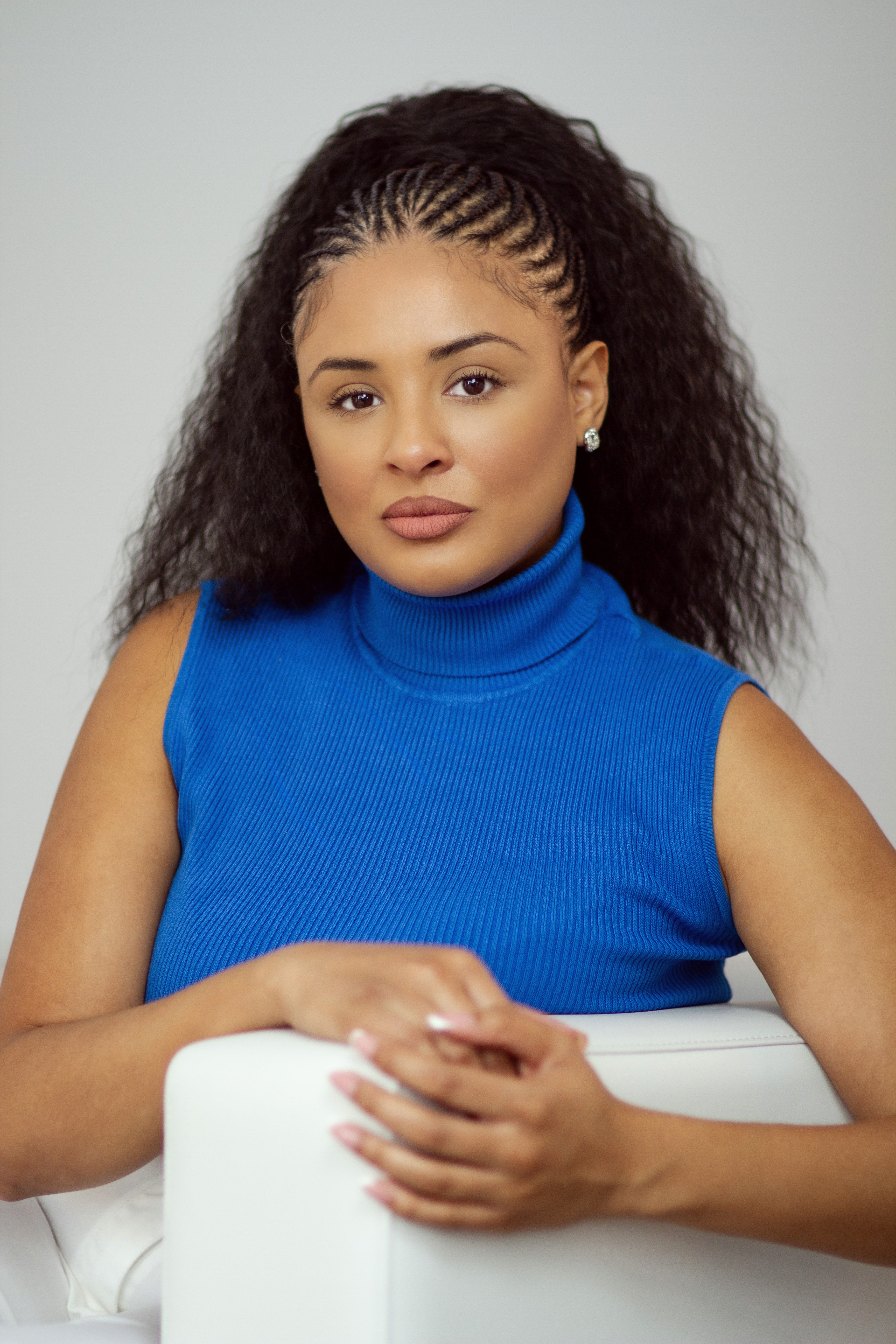 A young person with curly hair smiles at the camera while sitting in front of a laptop against a dark background.