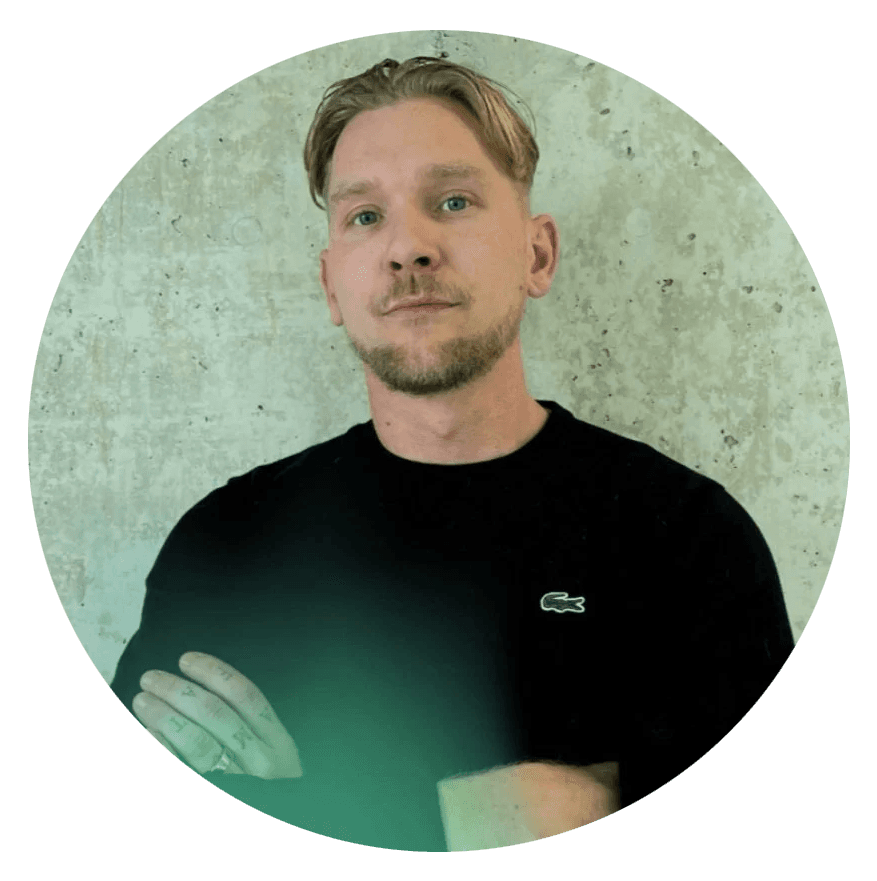 A person with short hair wearing a black shirt, standing confidently against a textured background.