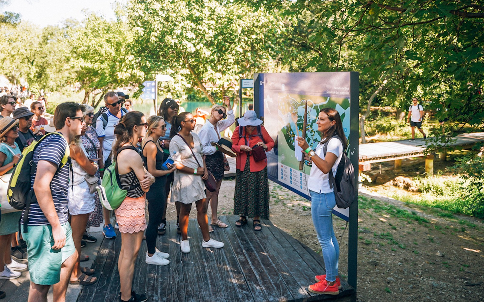 Grupo de turistas escuchando a un guía en el Parque Nacional de Krka, Croacia, cerca de un mapa indicador.