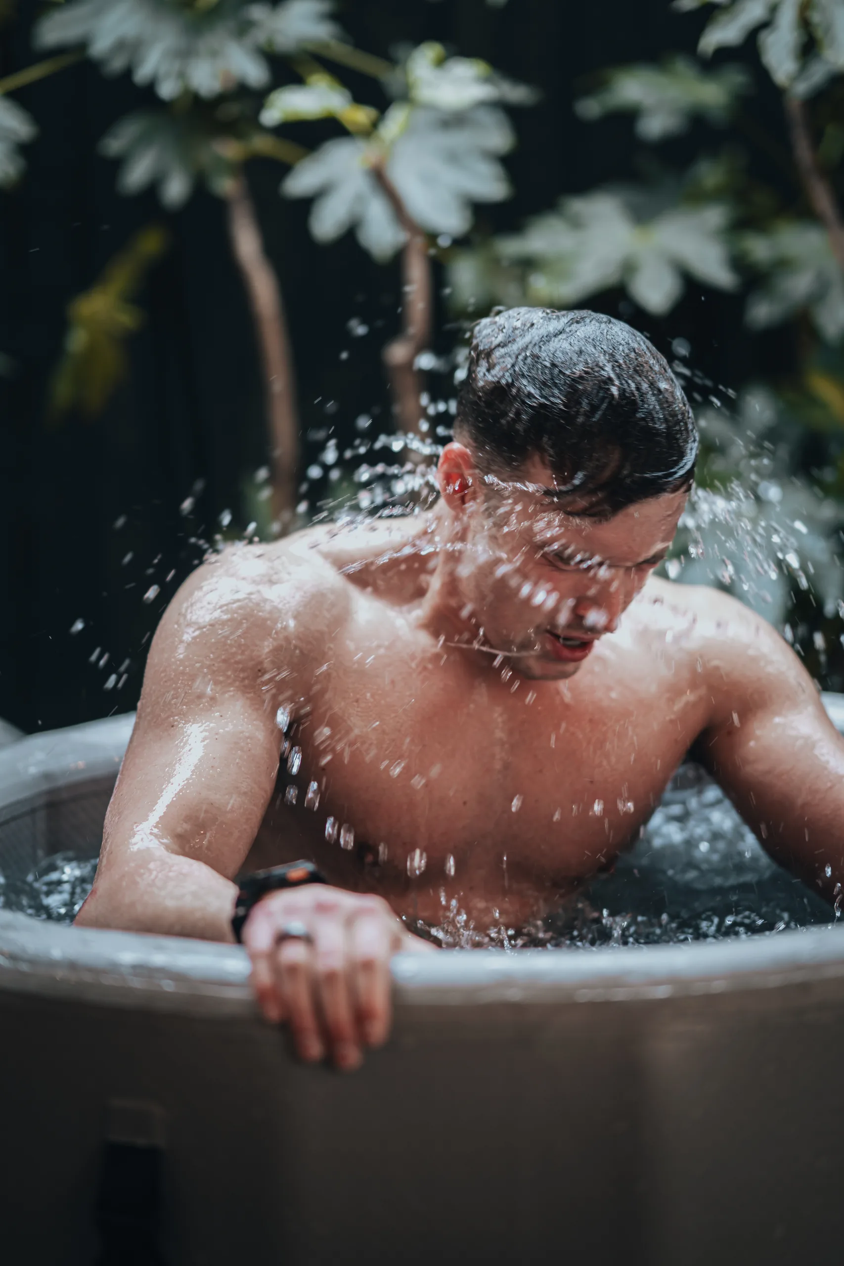 A man splashing water over himself in an ice bath surrounded by plants