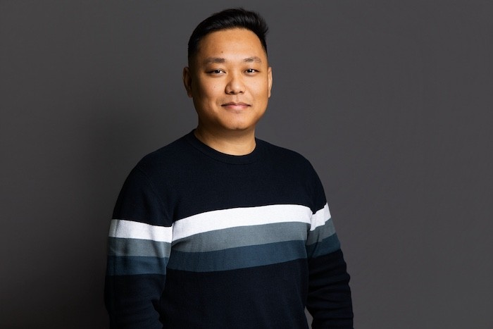 A young man in a white t-shirt stands against a light-colored background.