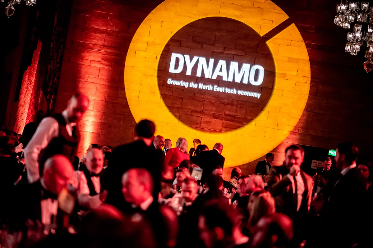 Image of the dynamo awards logo projected on a wall at the event with a room of people attending the event