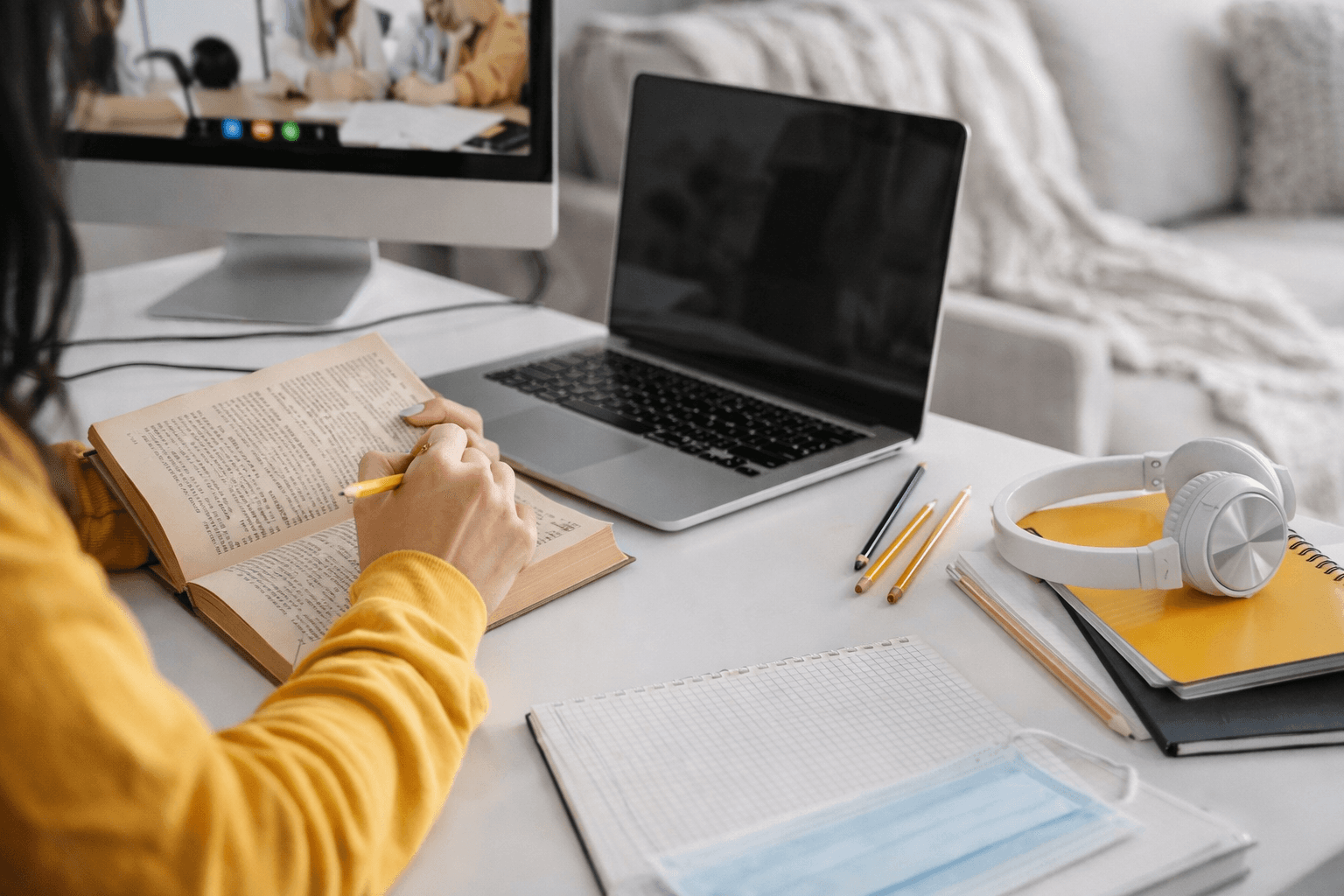 Masa başında kitap okuyan ve not alan bir öğrenci, yanında açık laptop, kulaklık ve defterlerle düzenli bir çalışma ortamında ders çalışıyor