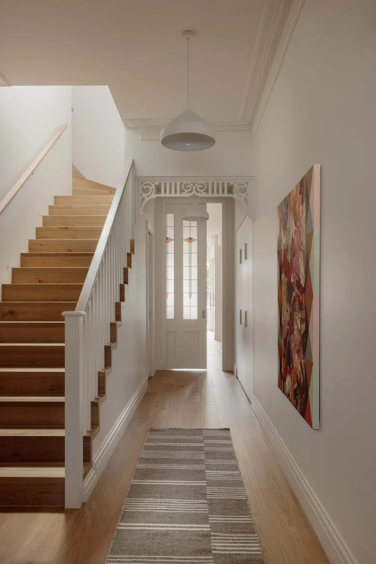 Modern hallway with wooden staircase, pendant light, and contemporary art.