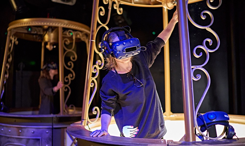 Guest wearing a virtual reality headset during an immersive entertainment experience, reaching towards an interactive display.