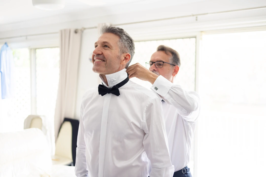 Best man putting black bow tie on groom