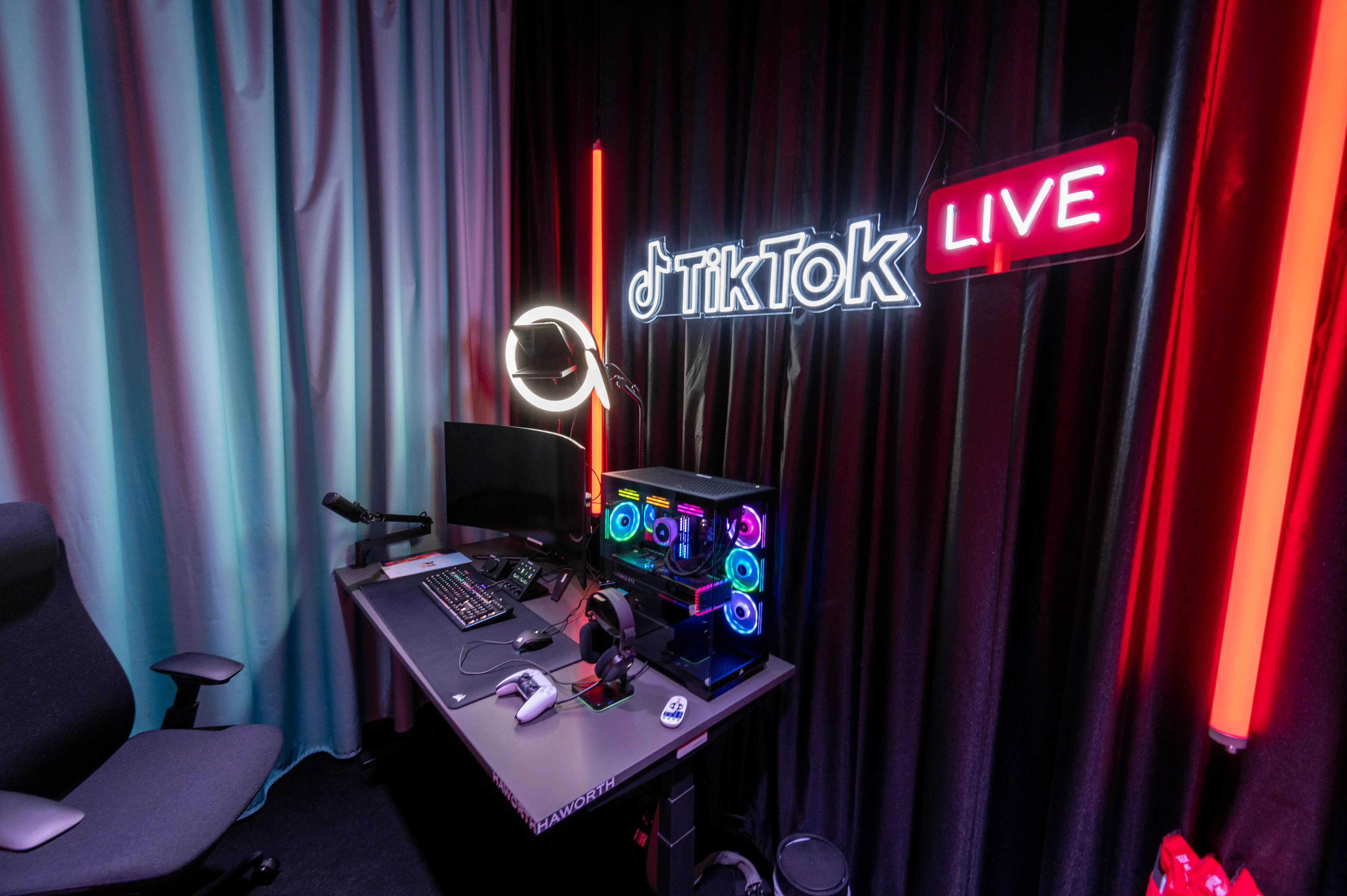 Streaming setup with RGB gaming PC and glowing TikTok Live neon sign between colorful light tubes at the Gamescom booth.