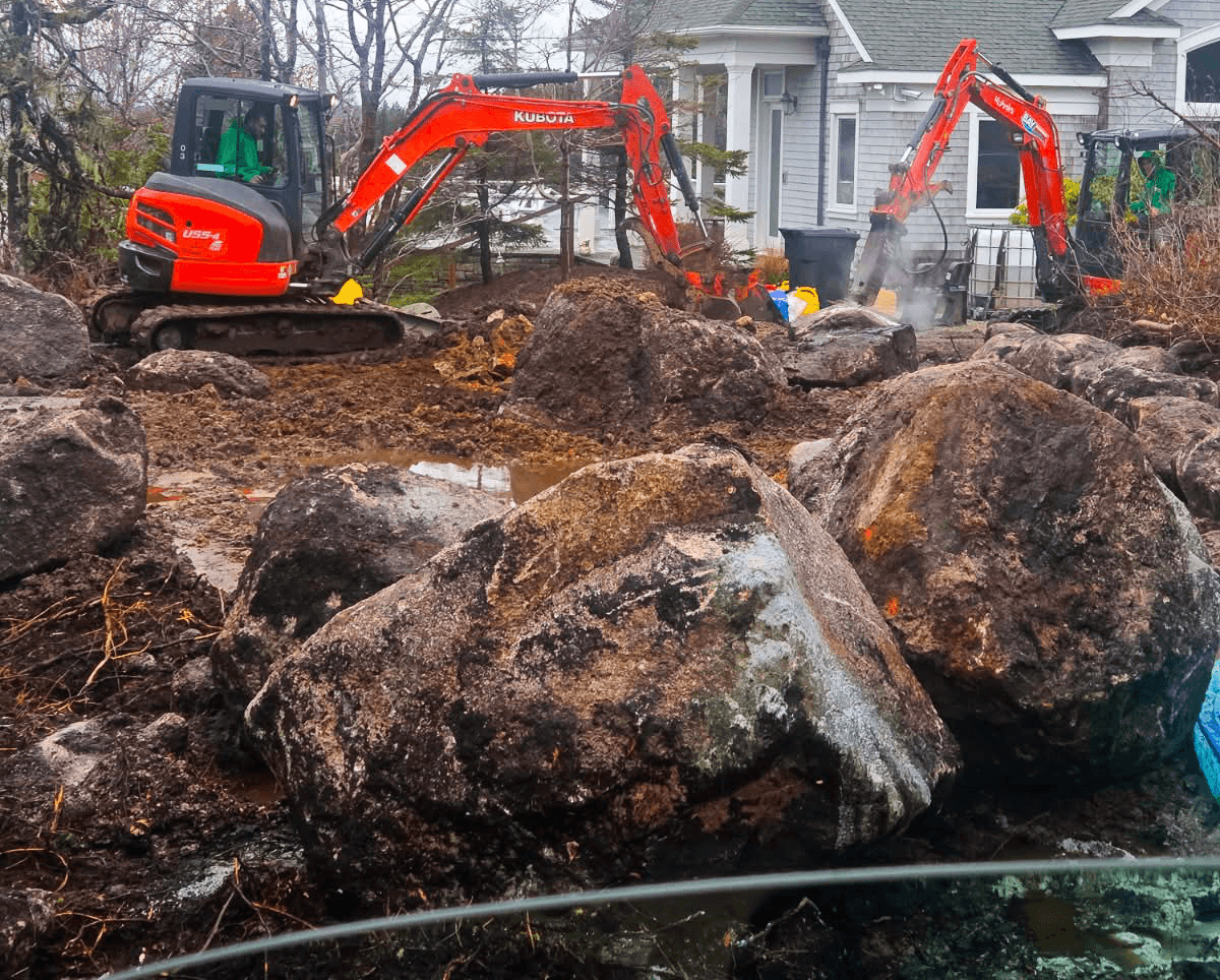 Excavator placing granite boulders and drainage base for a retaining wall near Halifax