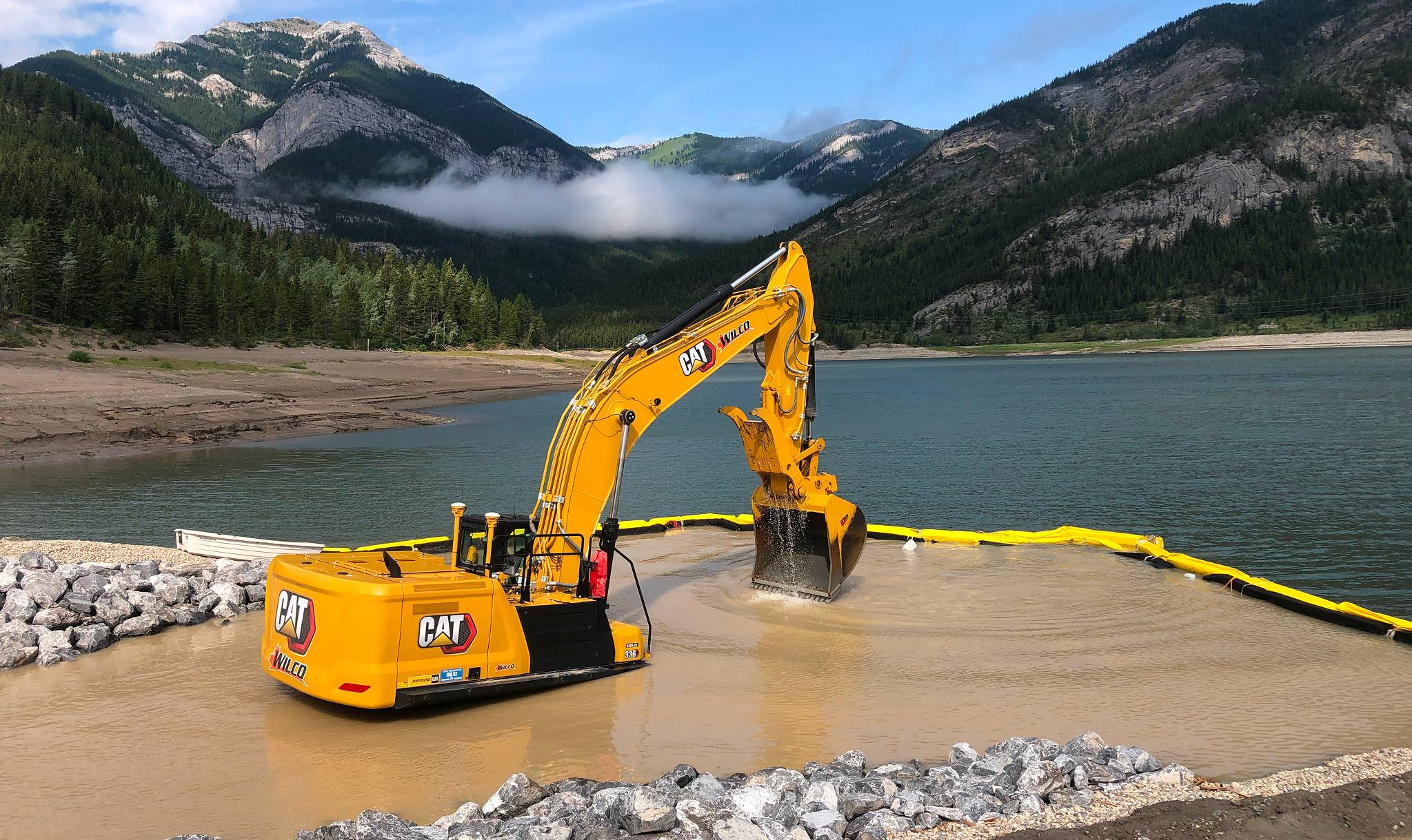 Excavator working on sediment removal at Barrier Lake with mountain backdrop in Kananaskis
